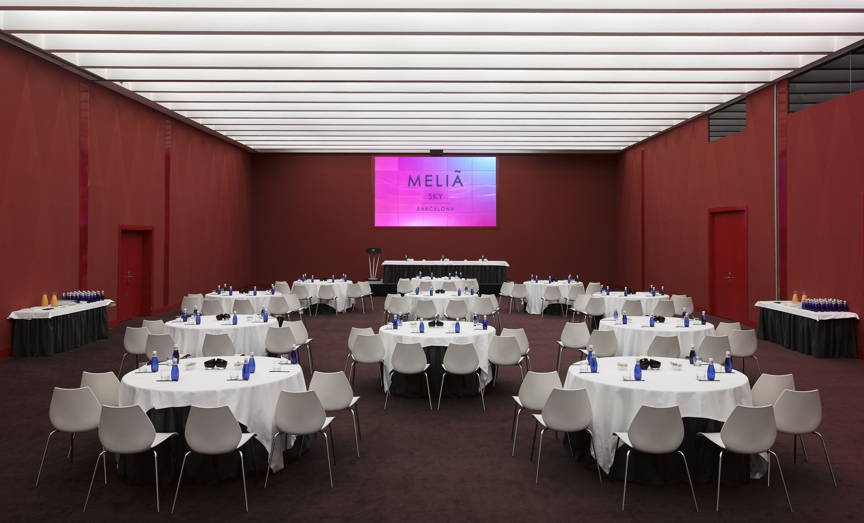 Melia Sky Barcelona meeting room, round tables, large screen, red walls.