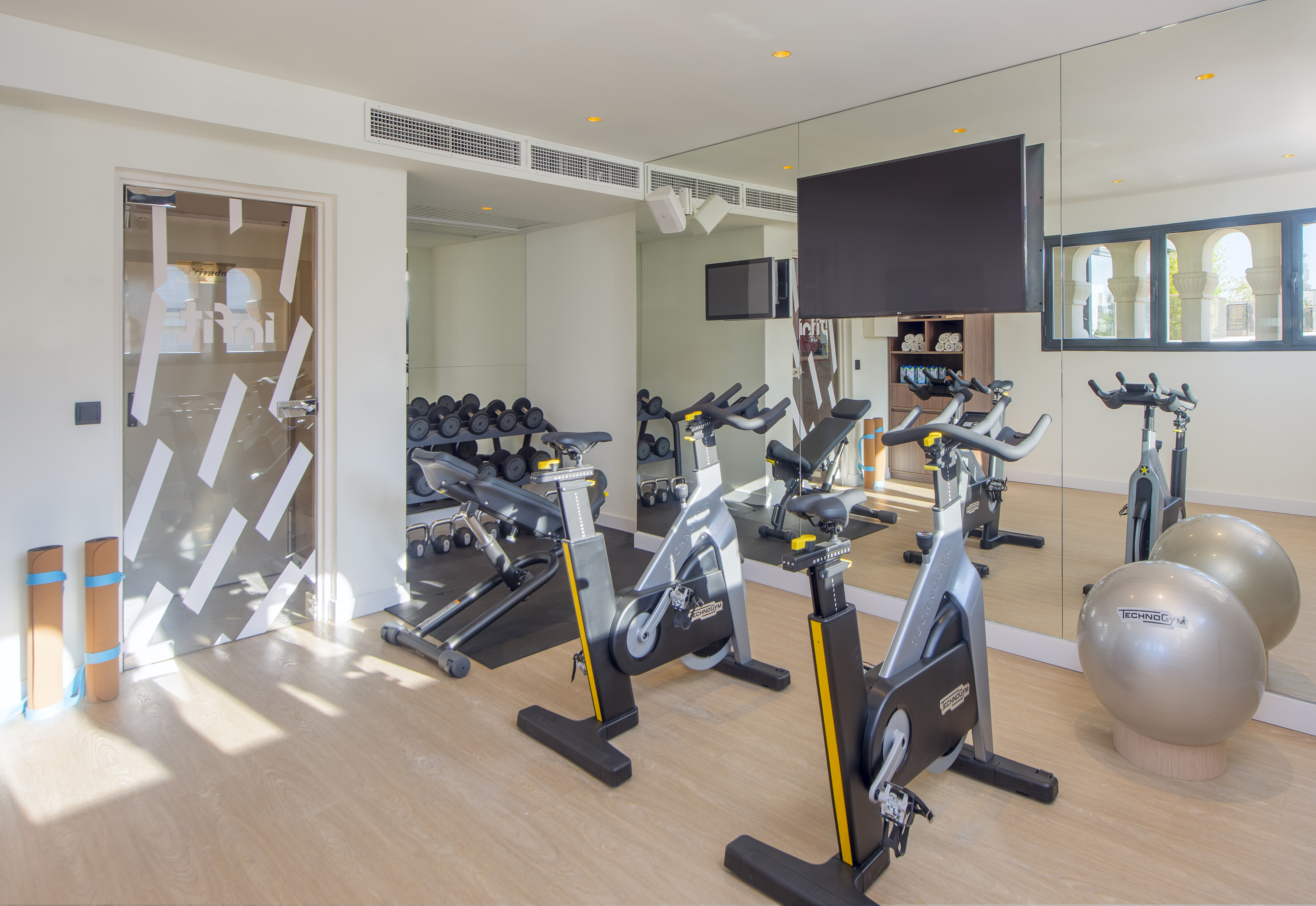 Modern gym with spin bikes, dumbbells, yoga mats, and large mirrors.