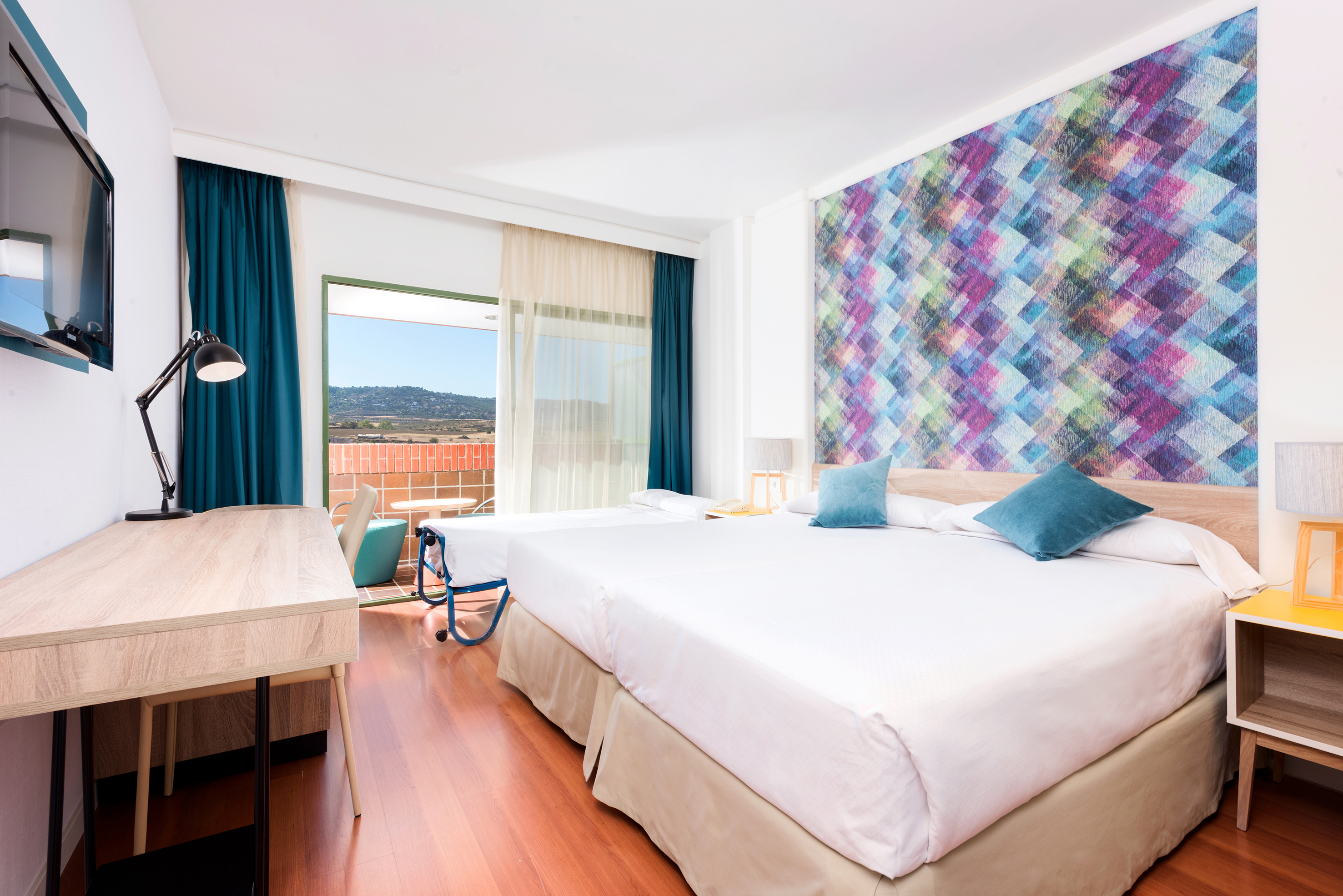 Modern hotel room with twin beds, rollaway, vibrant accent wall, balcony view.