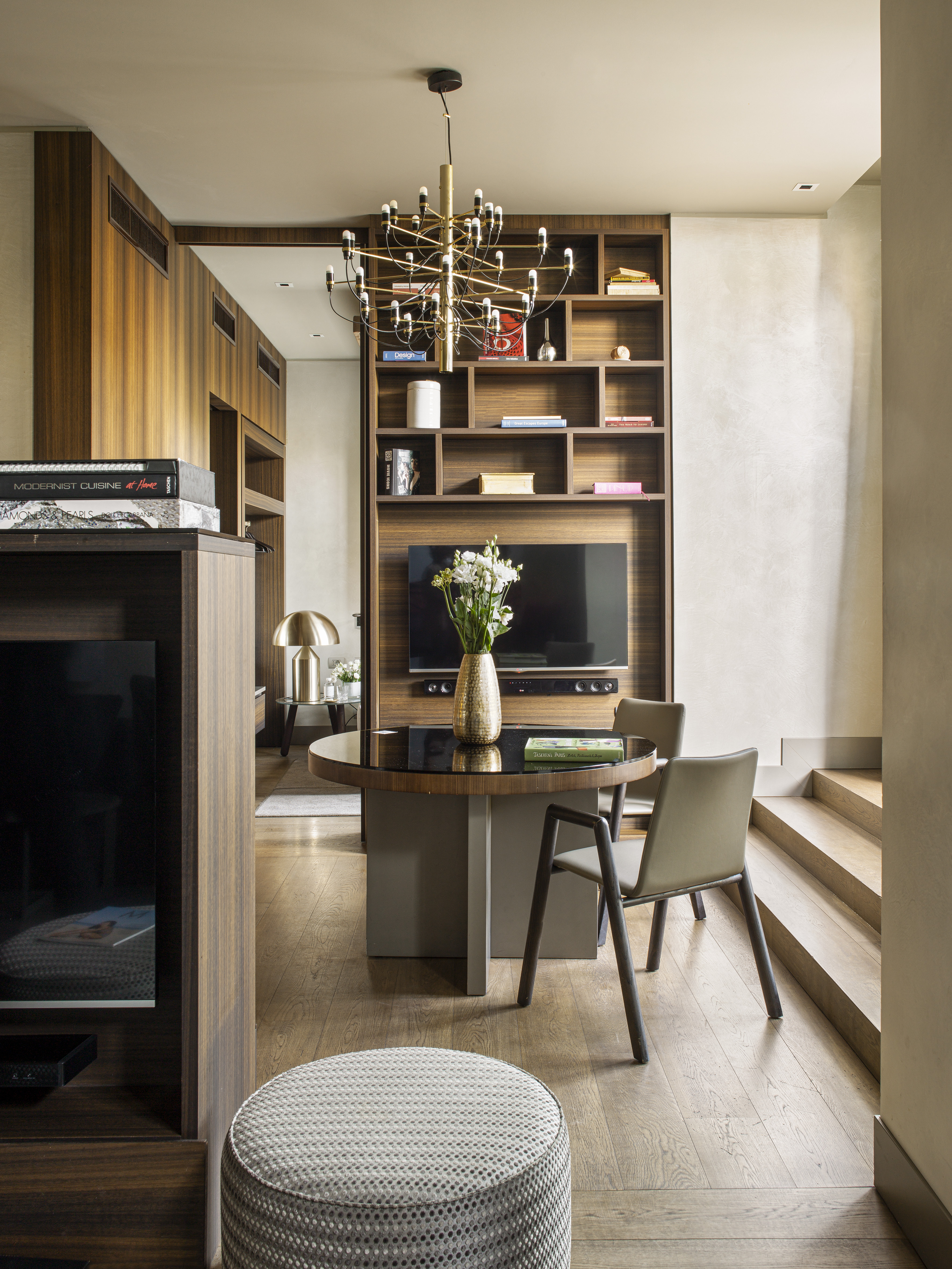 Modern dining area with round table, gold chandelier, wood media wall.