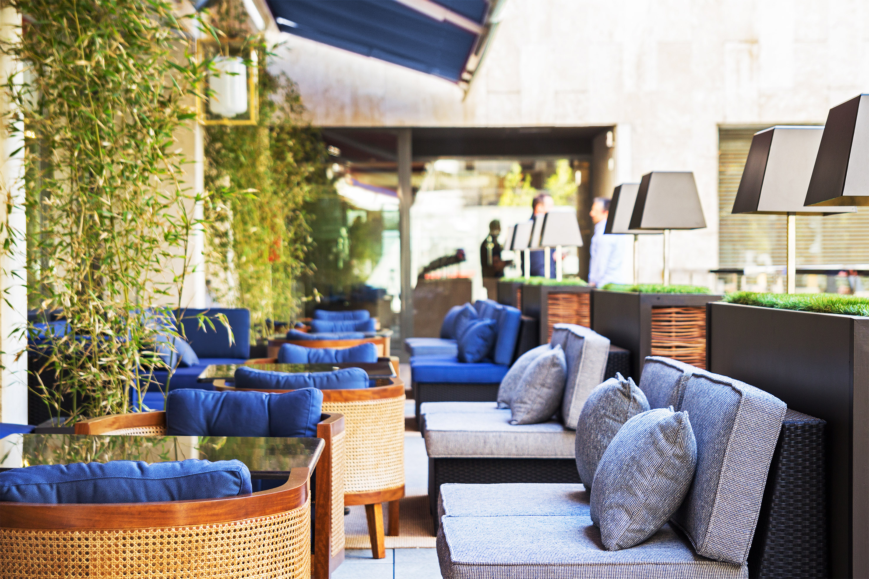 Outdoor patio lounge with blue cushioned seating, bamboo, and modern lamps.