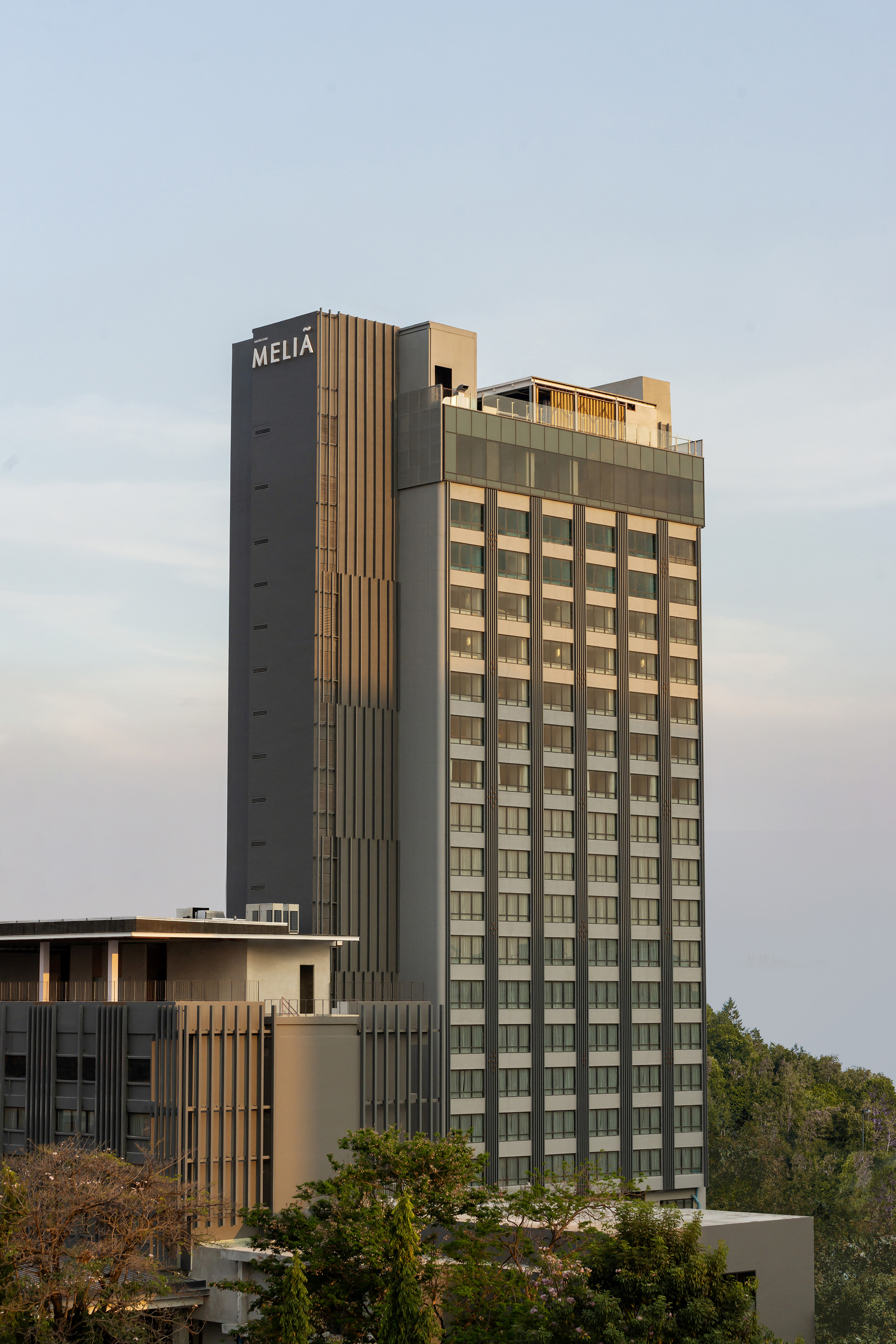 Meliá hotel building, modern grey high-rise with glass windows and trees.
