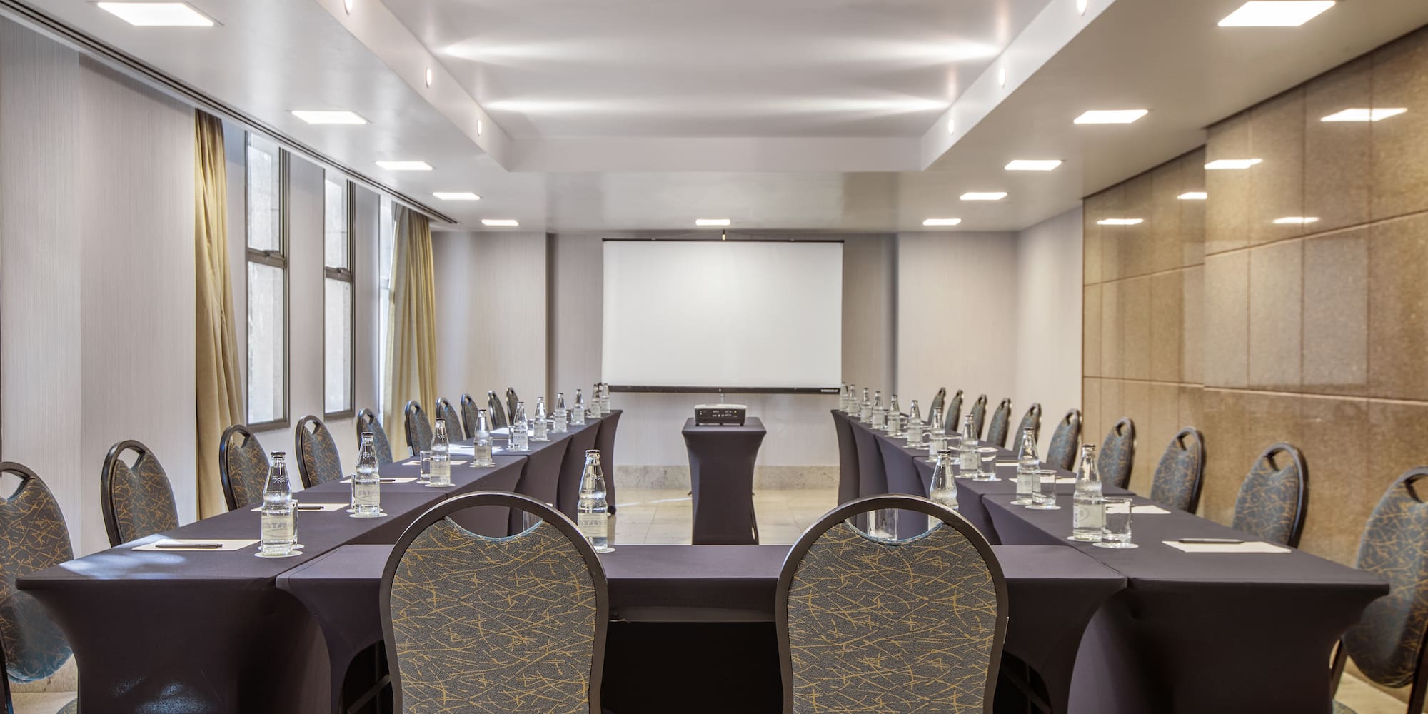 Empty U-shaped meeting room with projector screen, tables, and modern chairs.