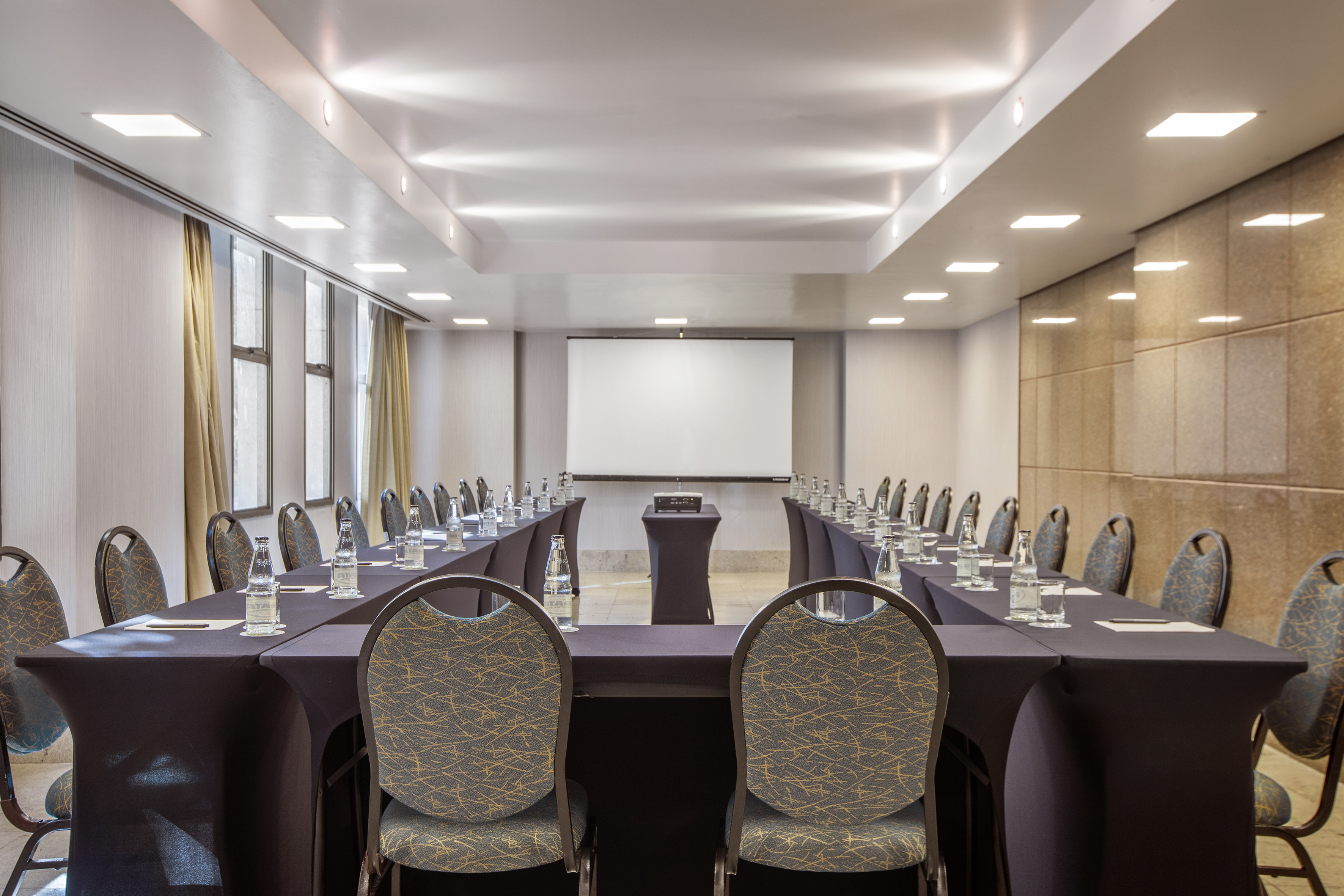 Empty U-shaped meeting room with projector screen, tables, and modern chairs.