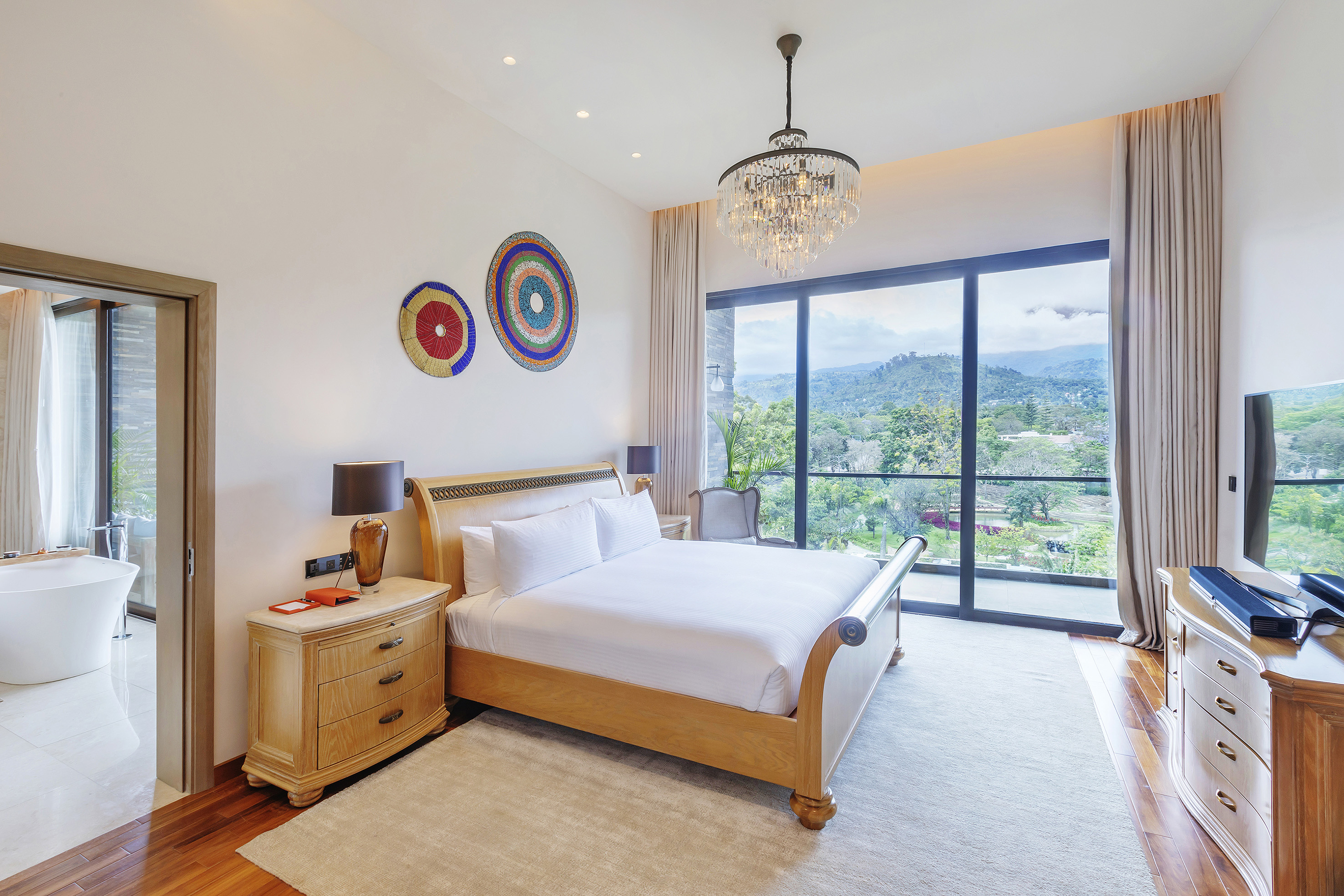 Modern luxury bedroom with a wooden sleigh bed, mountain view, and chandelier.