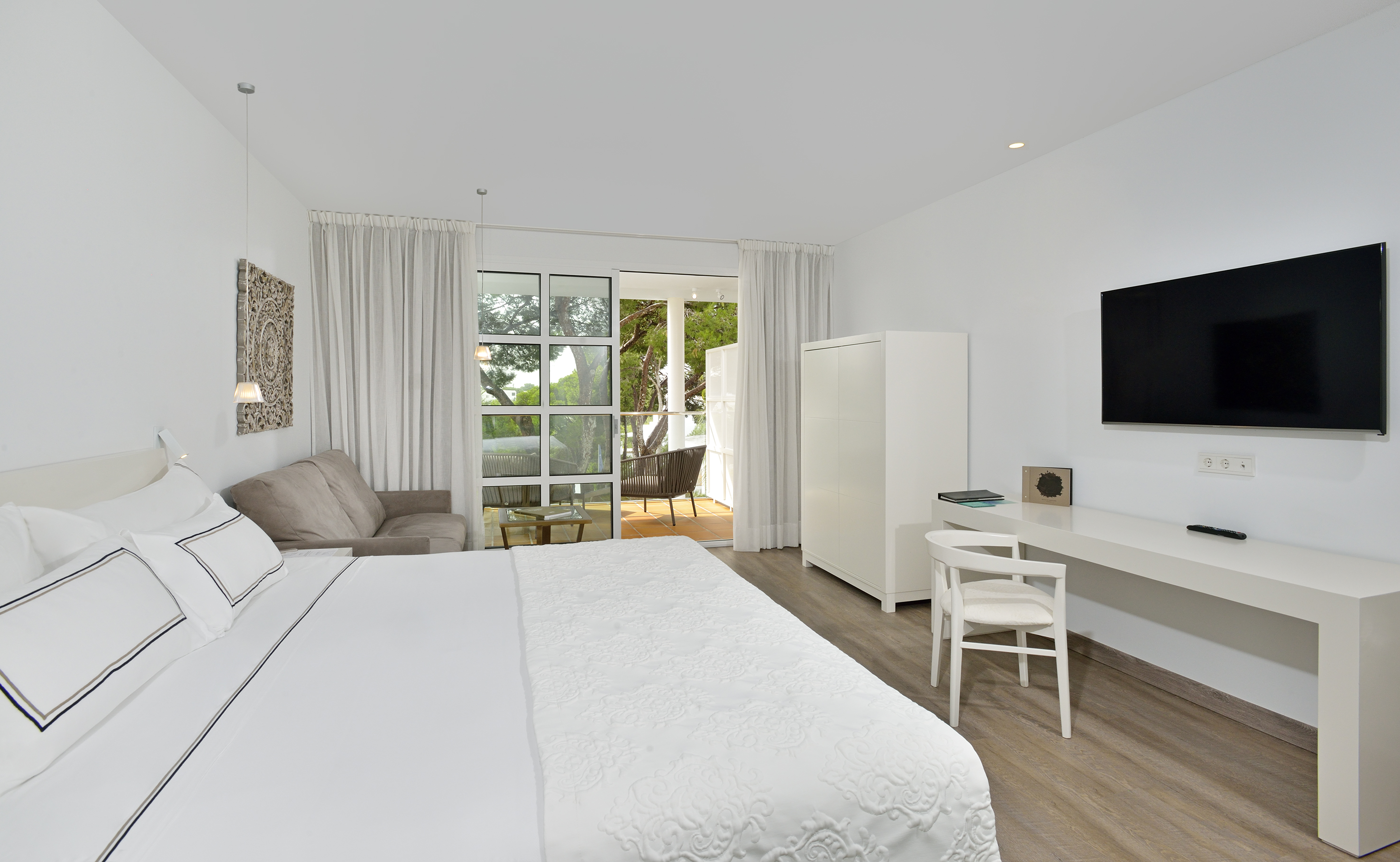 Bright, modern hotel bedroom with white decor, sofa, and private balcony.