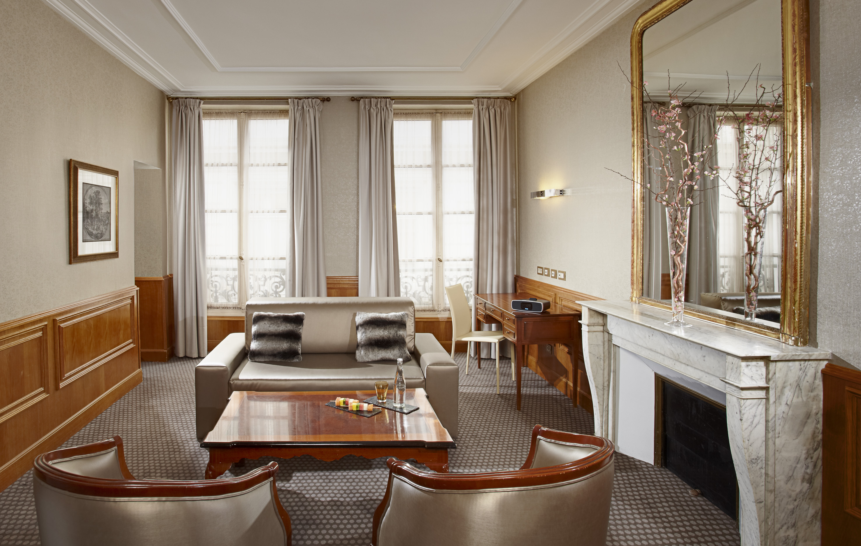 Elegant hotel suite with sofa, desk, fireplace, and large mirror.
