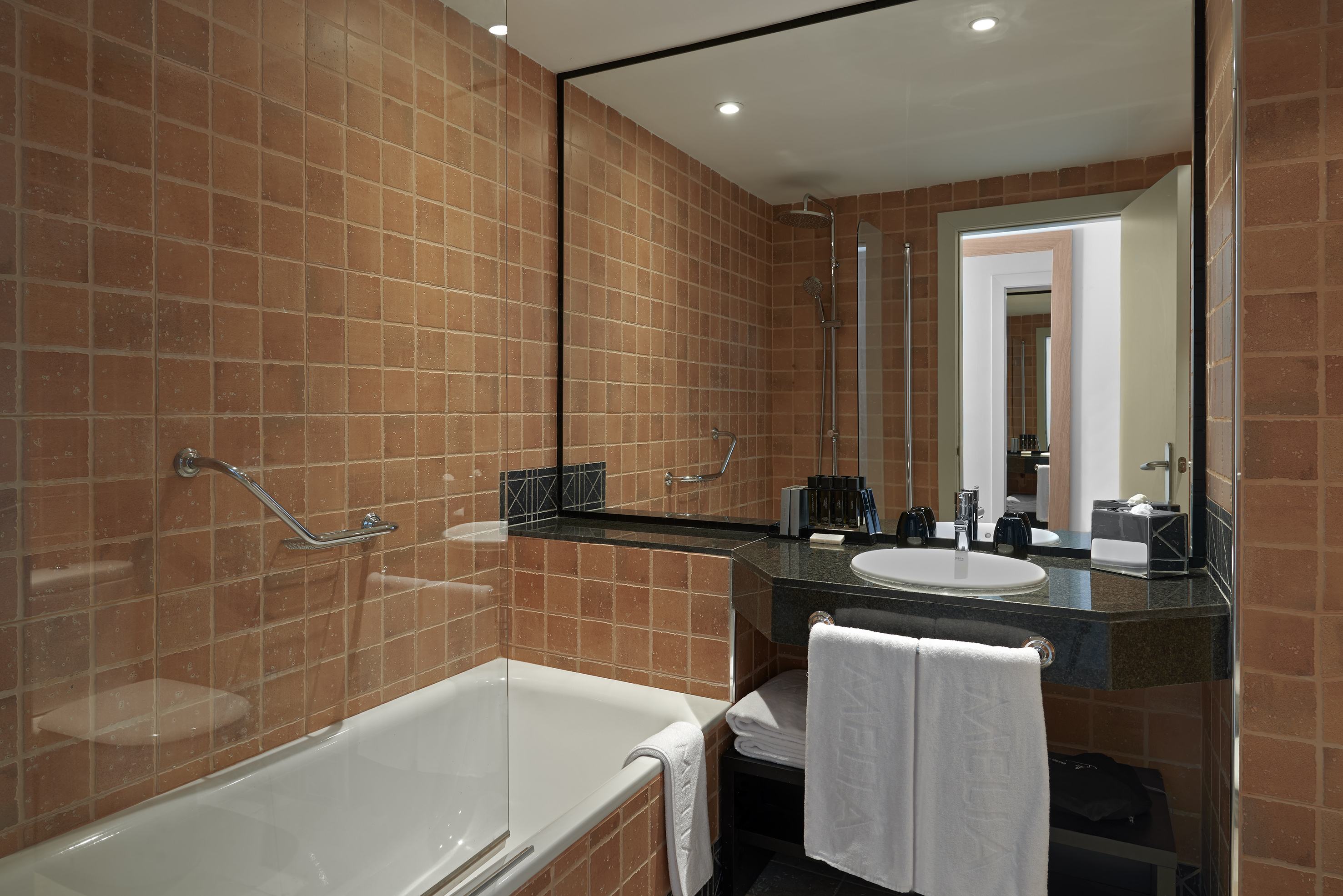 Hotel bathroom with terracotta tiles, bathtub, glass shower, and vanity sink.
