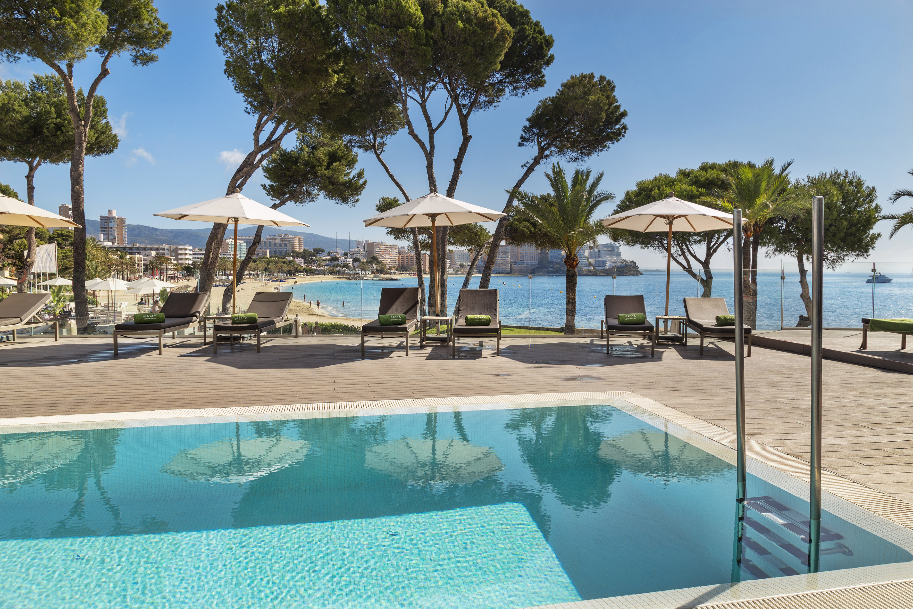 a pool with umbrellas and chairs on a deck by a beach