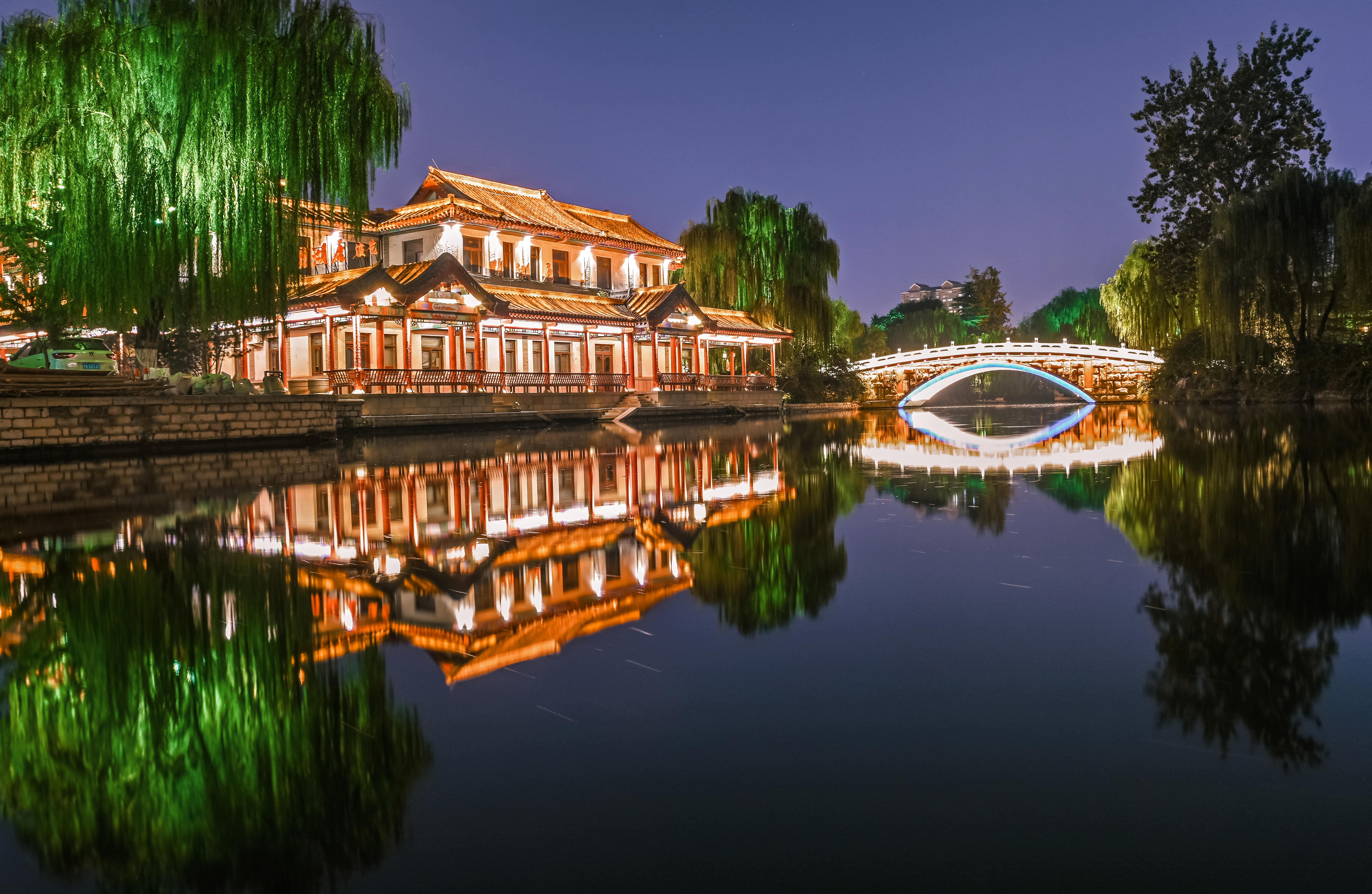 a building with lights on it and a bridge over water