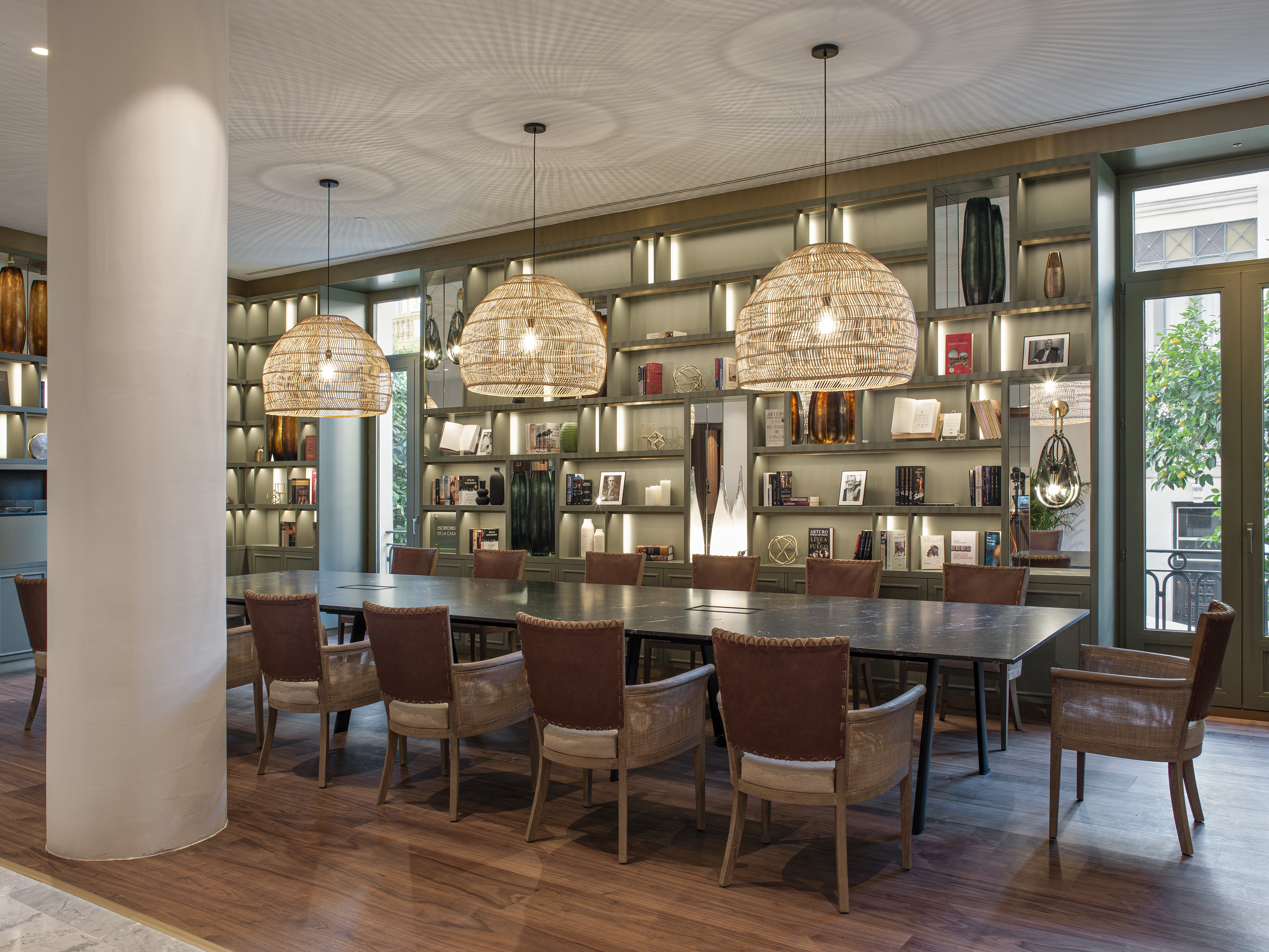 Meeting room with long table, leather chairs, rattan pendants, and lit library wall.