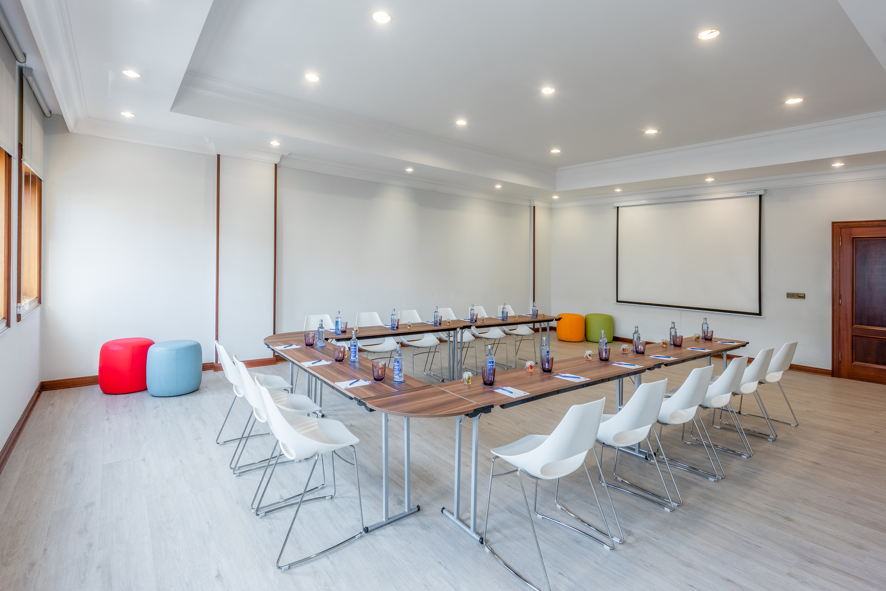 Modern U-shape meeting room with white chairs, projector screen, and colorful accents.