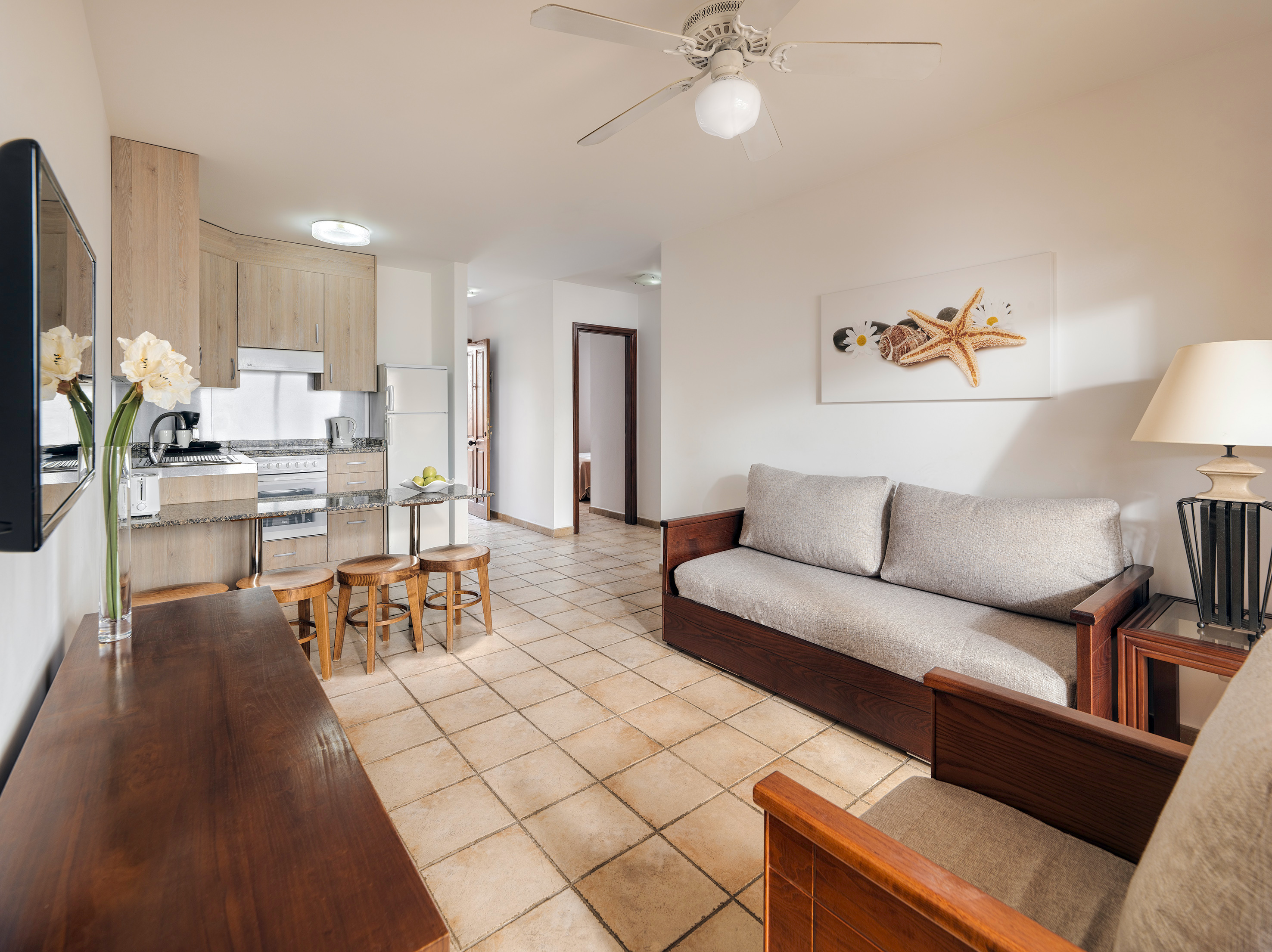 Bright open-plan apartment living space with kitchen, sofa, and beach decor.