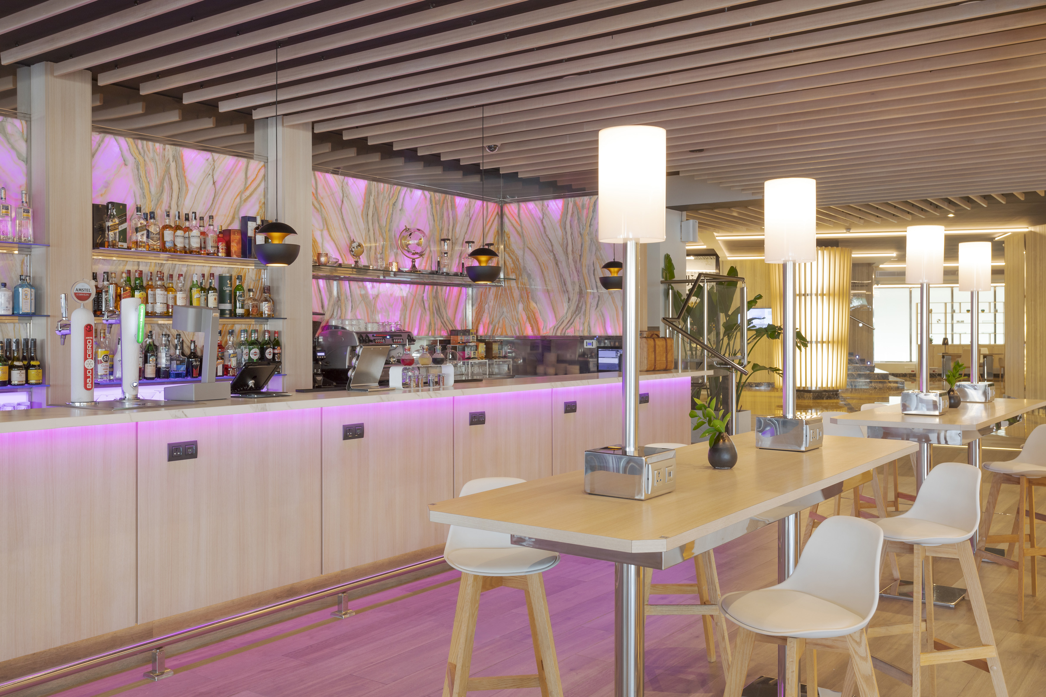 Modern hotel bar with pink backlit marble and high tables.