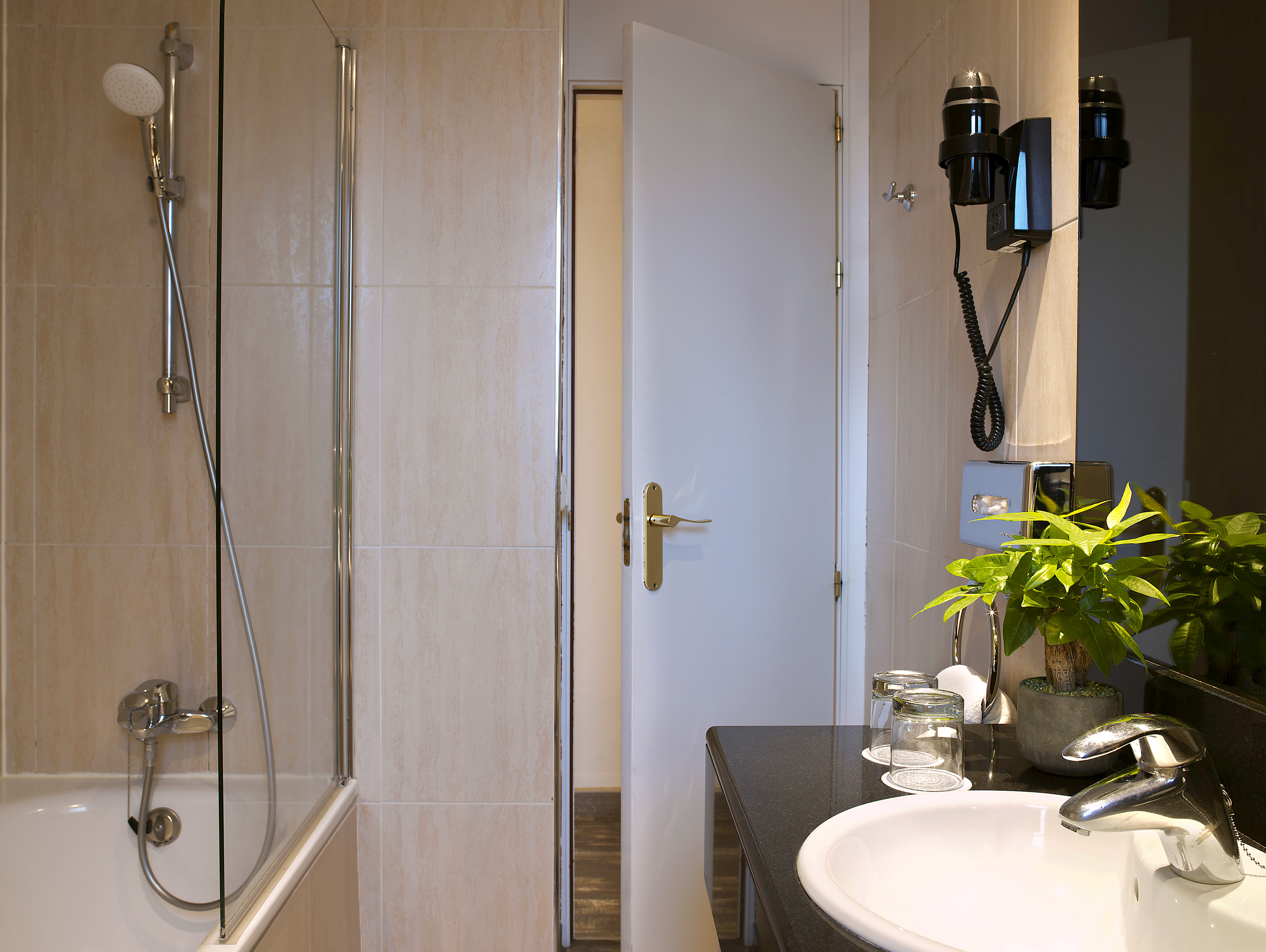 Hotel bathroom with shower, bathtub, sink, and wall-mounted hairdryer.