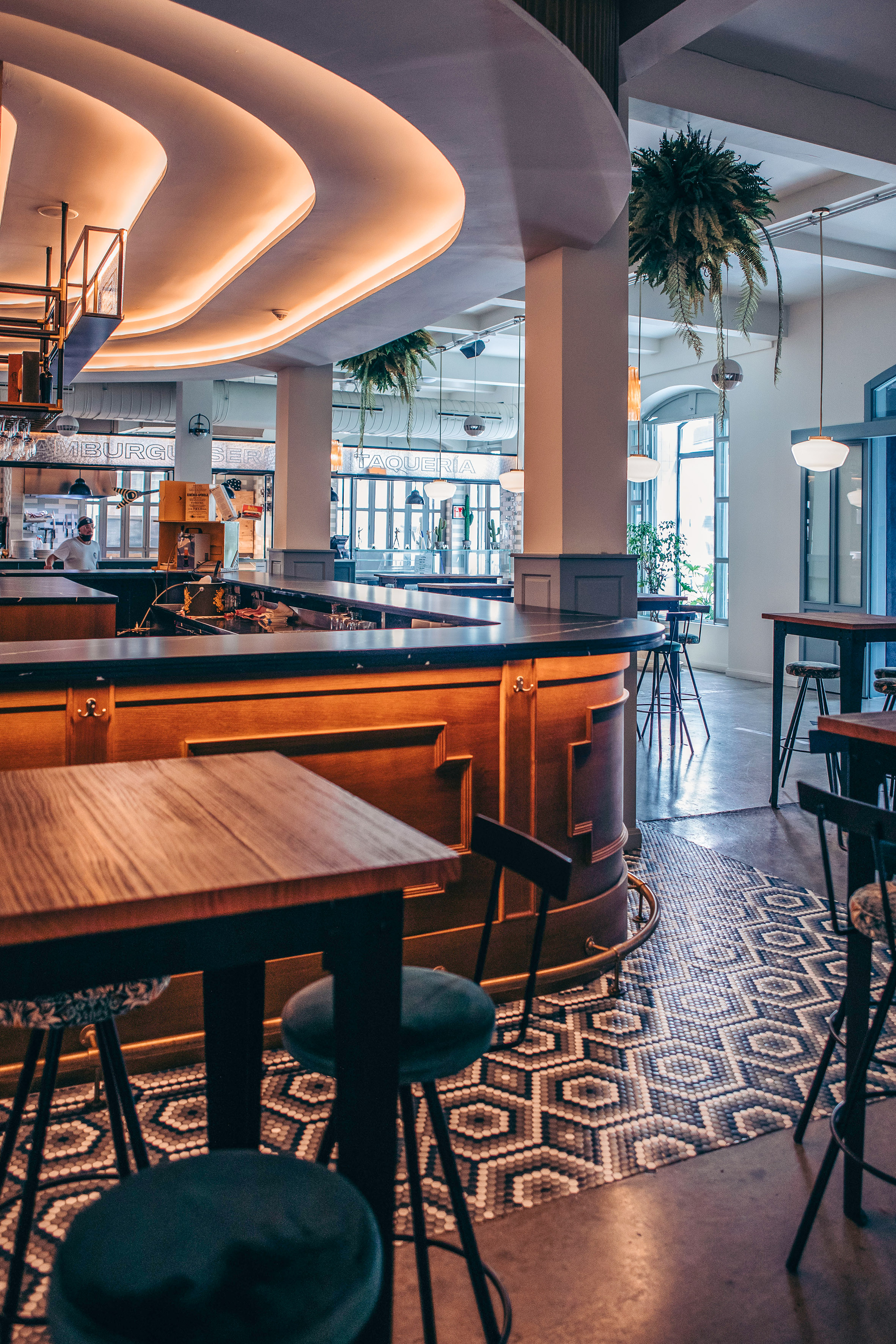 Modern food hall bar with glowing curved ceiling, geometric floor, and sleek seating.