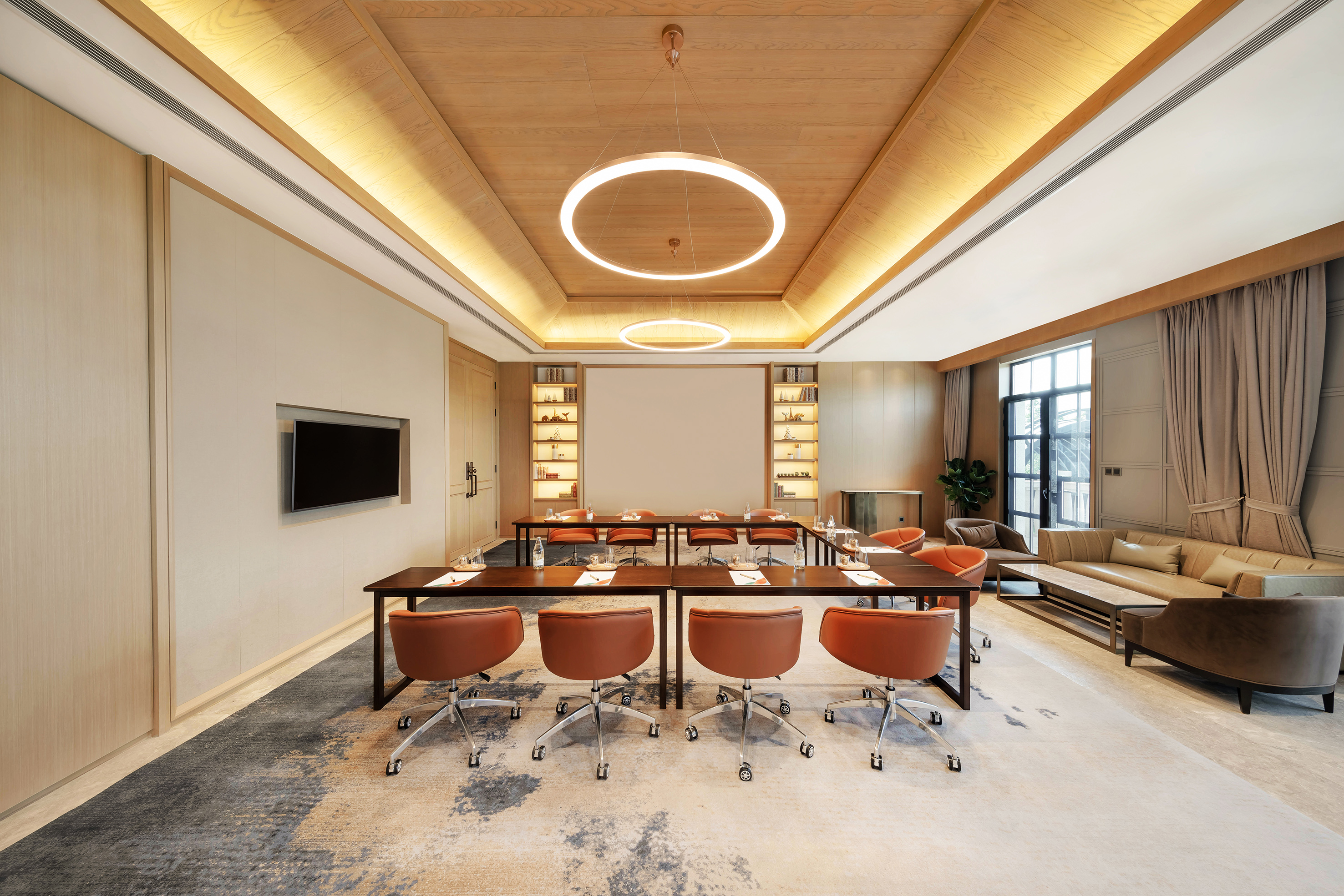 Modern corporate meeting room with tables, leather chairs, TV, and lounge.