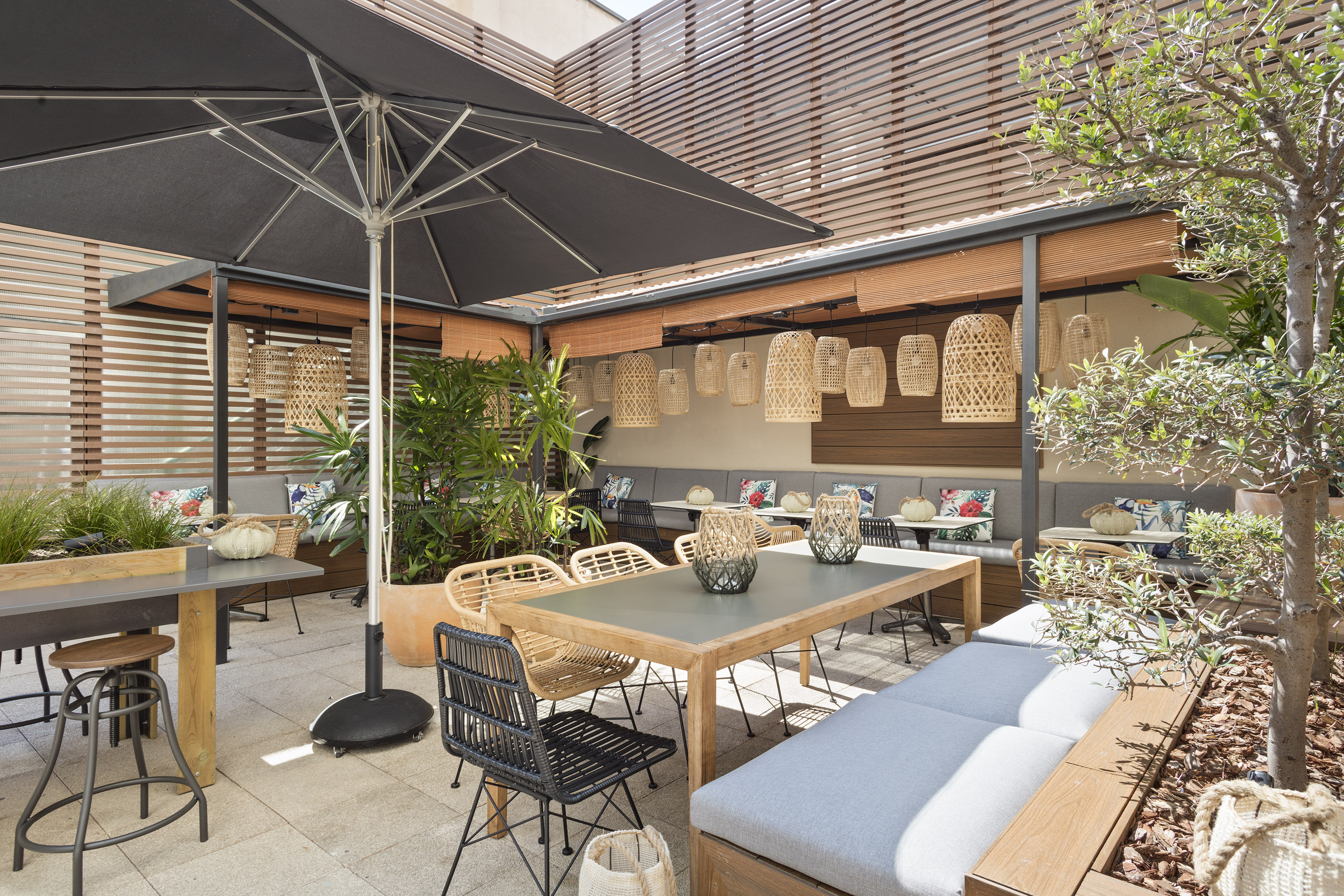 Modern outdoor dining patio with black umbrella, wooden furniture, and rattan lights.