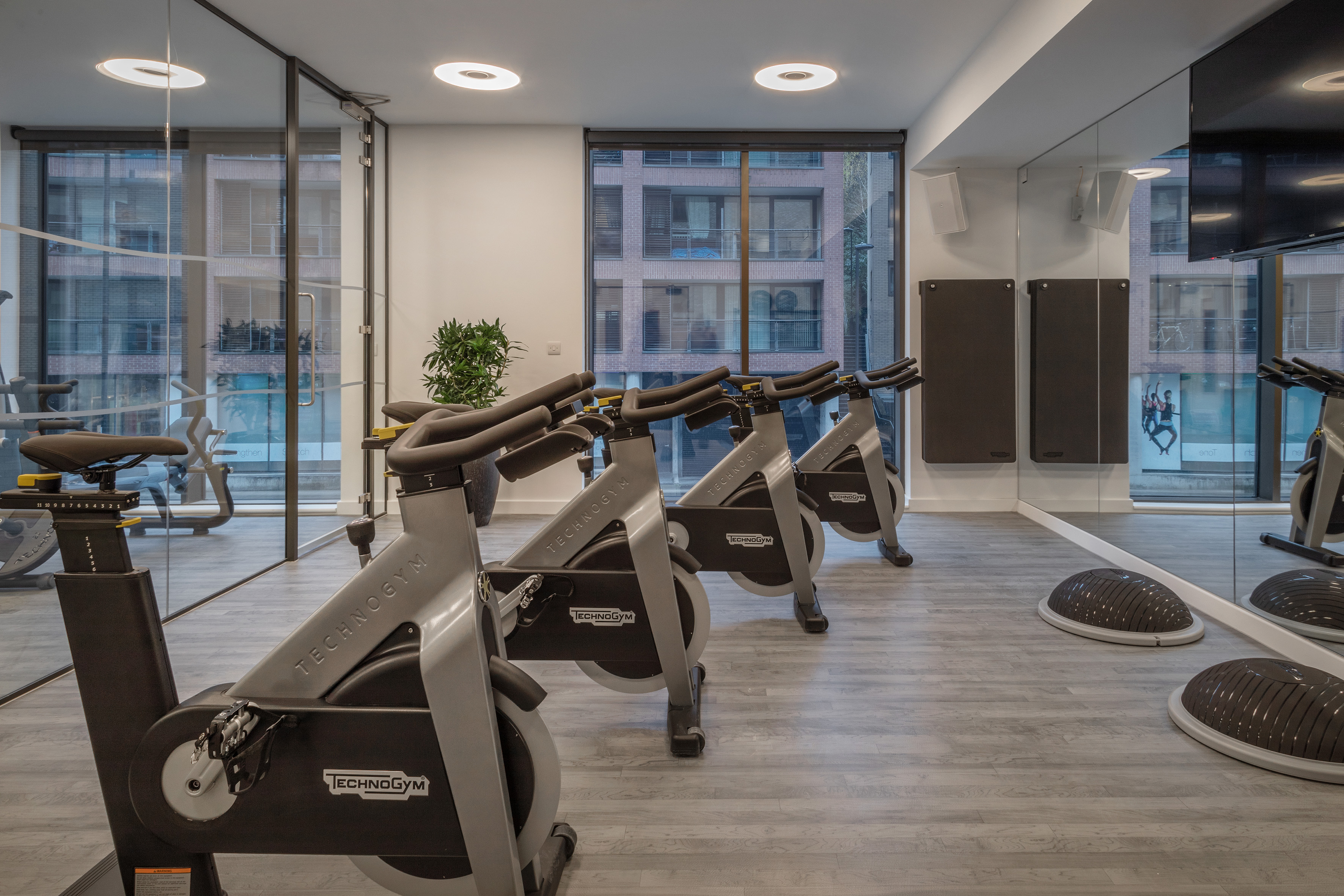 Row of Technogym spin bikes in a modern gym studio with large windows.