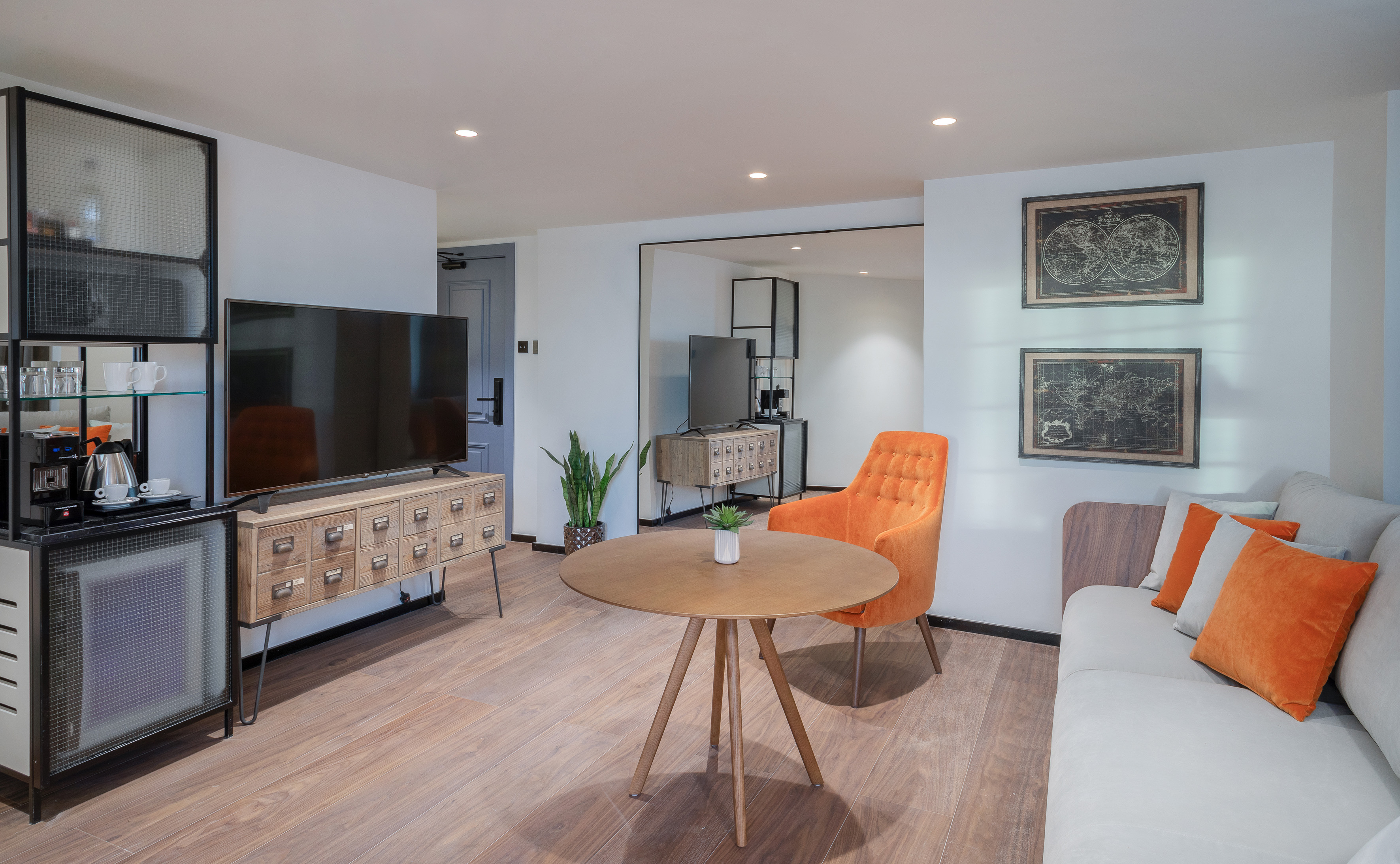 Modern hotel suite living room with orange chair, grey sofa, TV, and coffee bar.