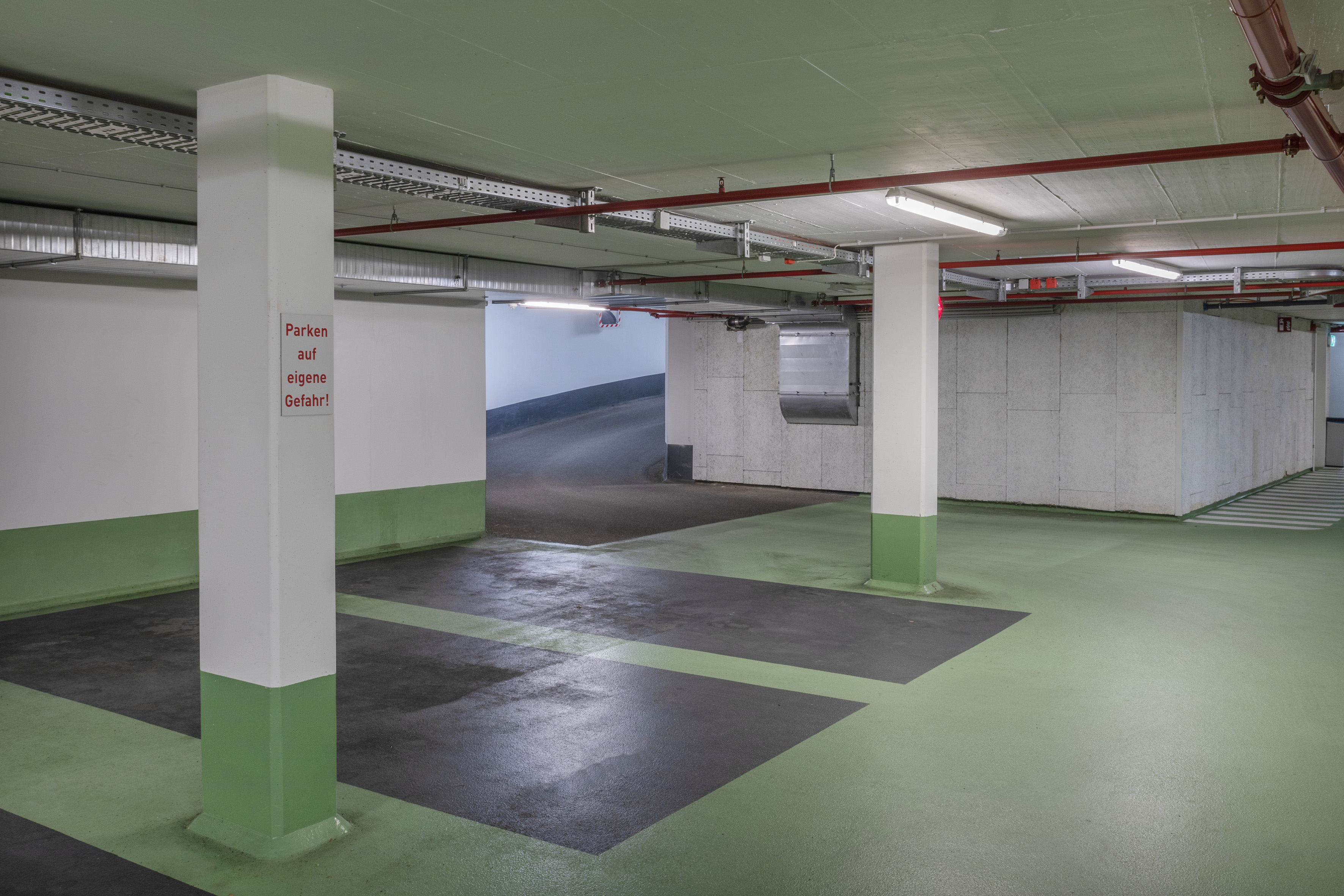 Empty underground parking garage with green floor markings and concrete columns.