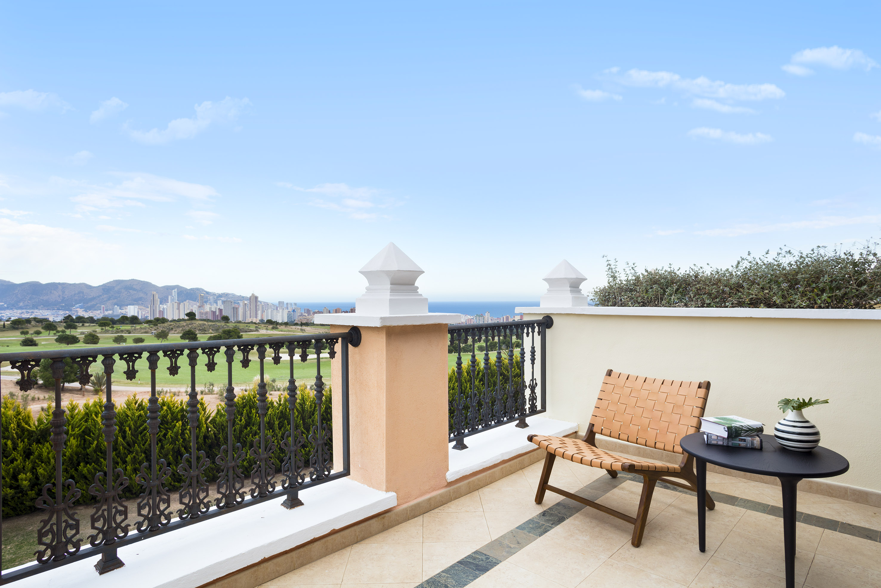 Balcony overlooking golf course, city skyline, and sea with outdoor seating.