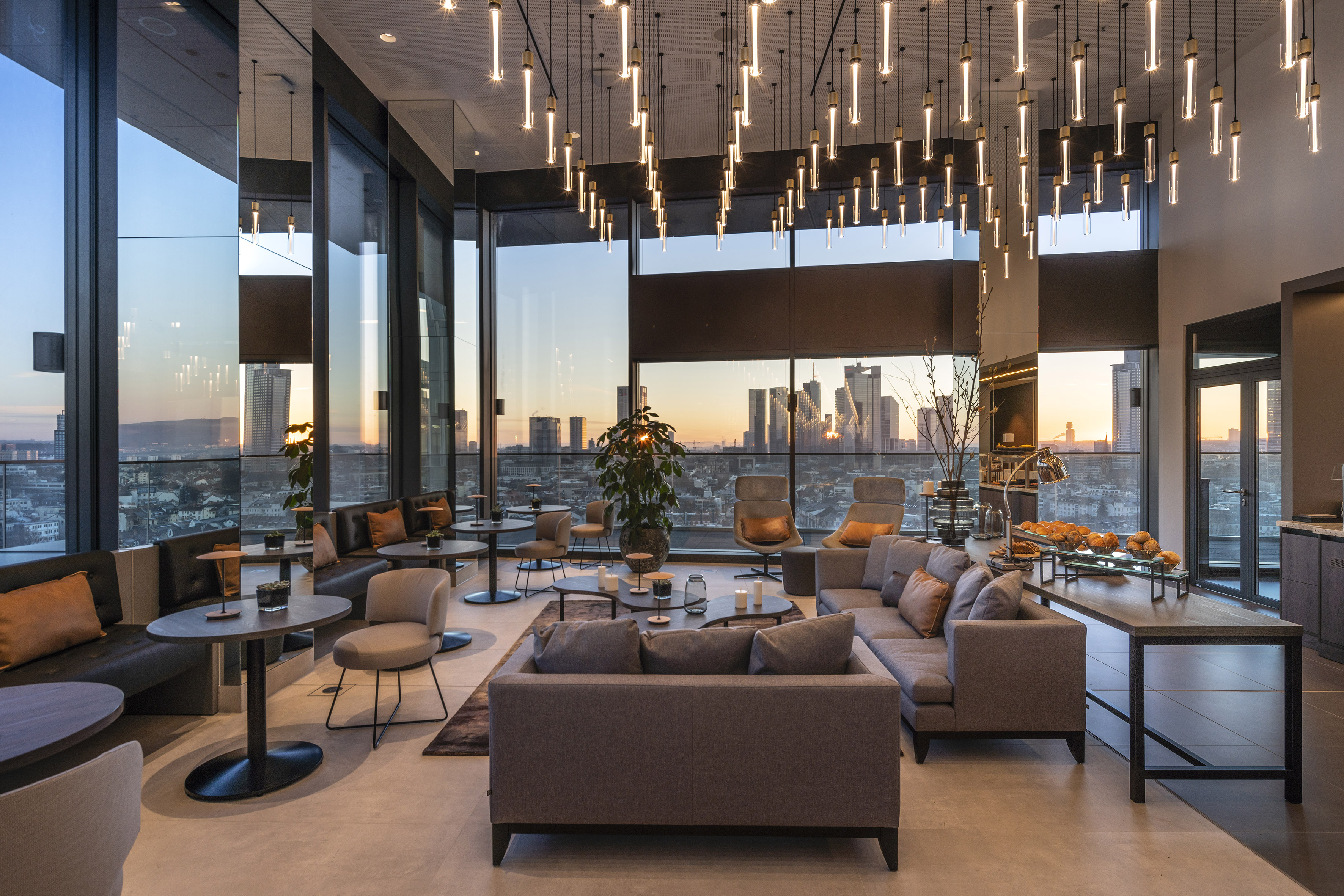 Modern hotel lounge with panoramic city sunset view and elegant pendant lights.
