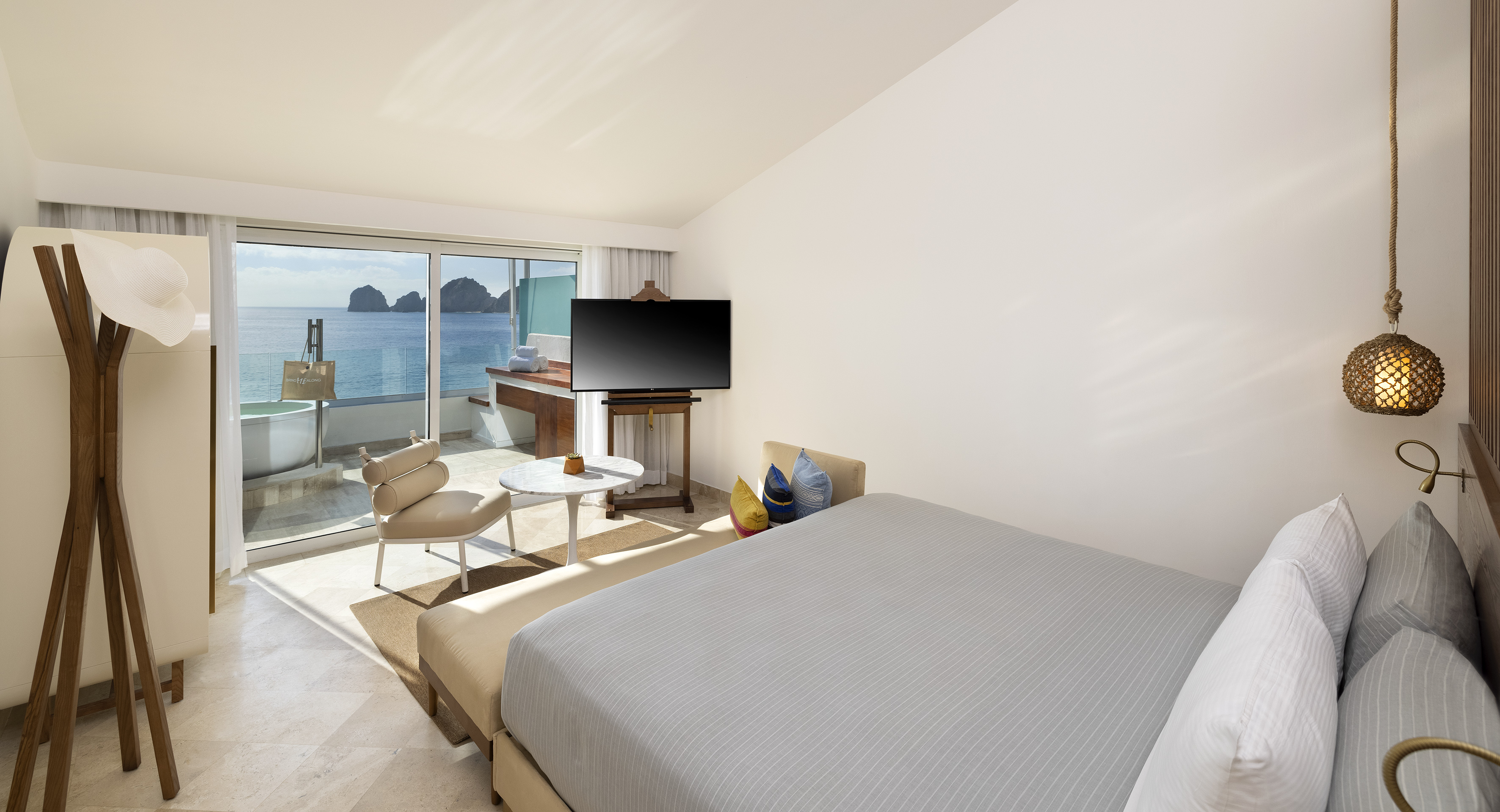 Modern hotel bedroom with ocean view, balcony bathtub, and easel TV.
