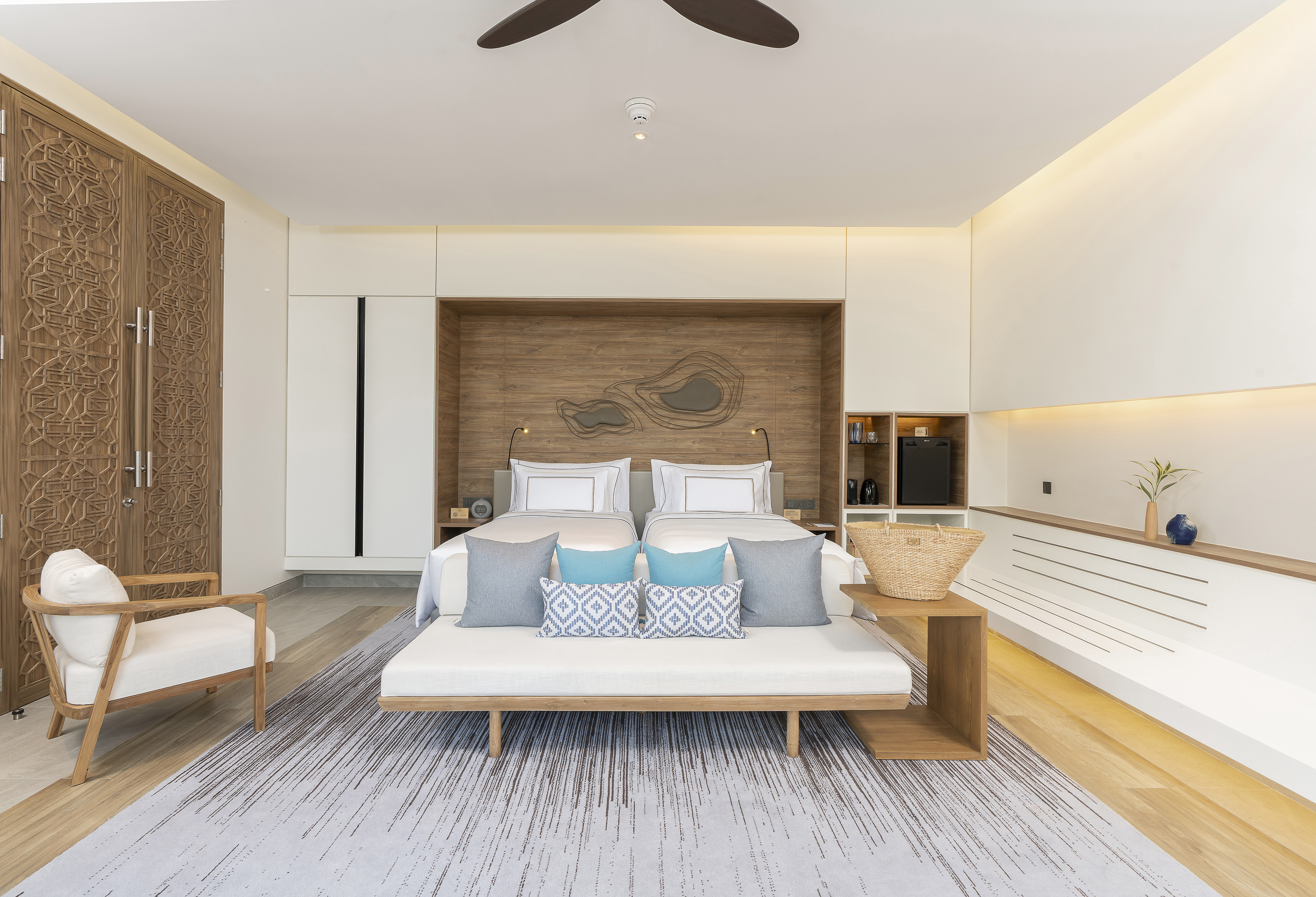 Modern hotel room with king bed, carved wood wardrobe, and minimalist decor.