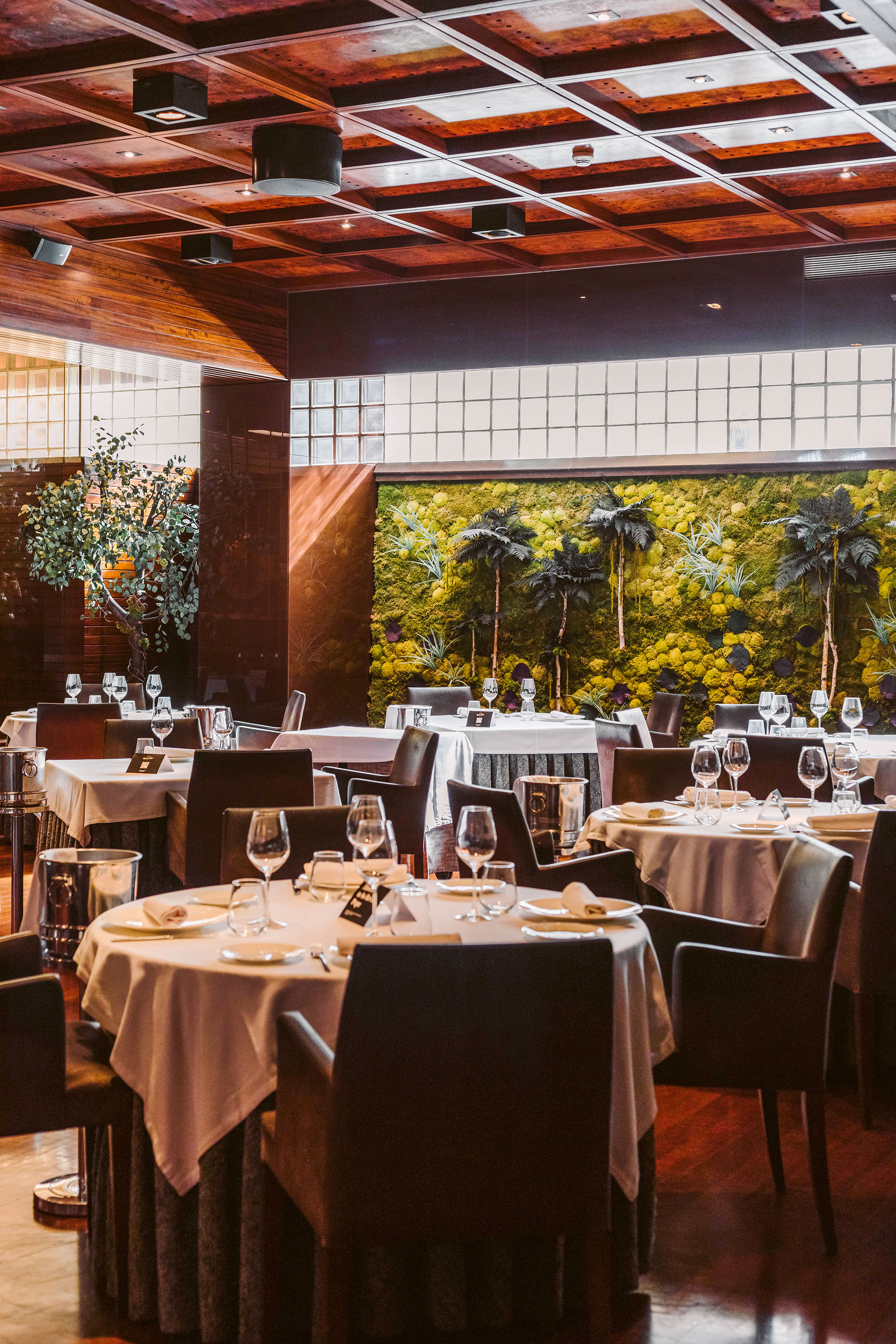Elegant fine dining restaurant interior with set tables and a striking moss wall.