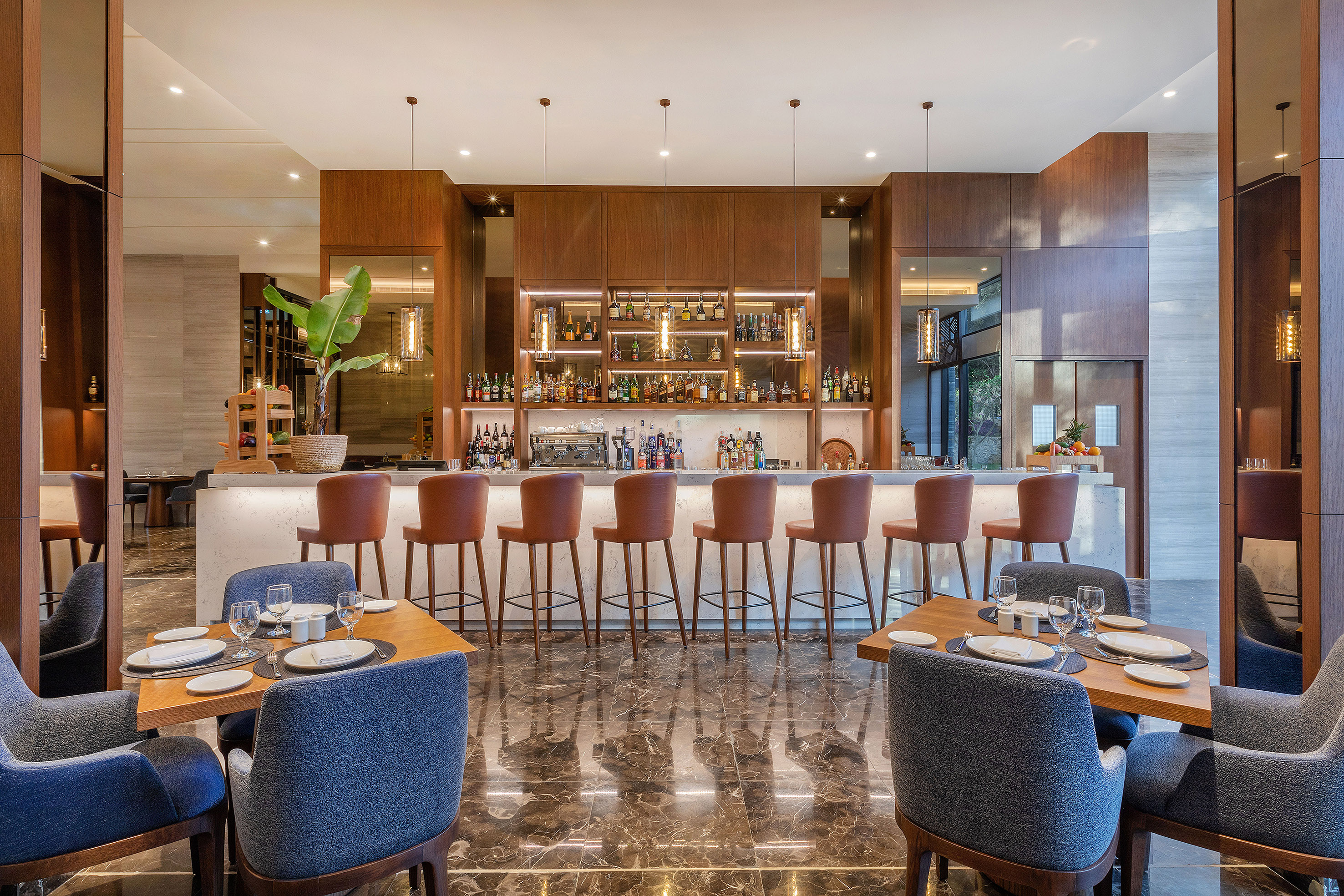 Elegant hotel bar and restaurant with liquor bottles, bar stools, and dining tables.
