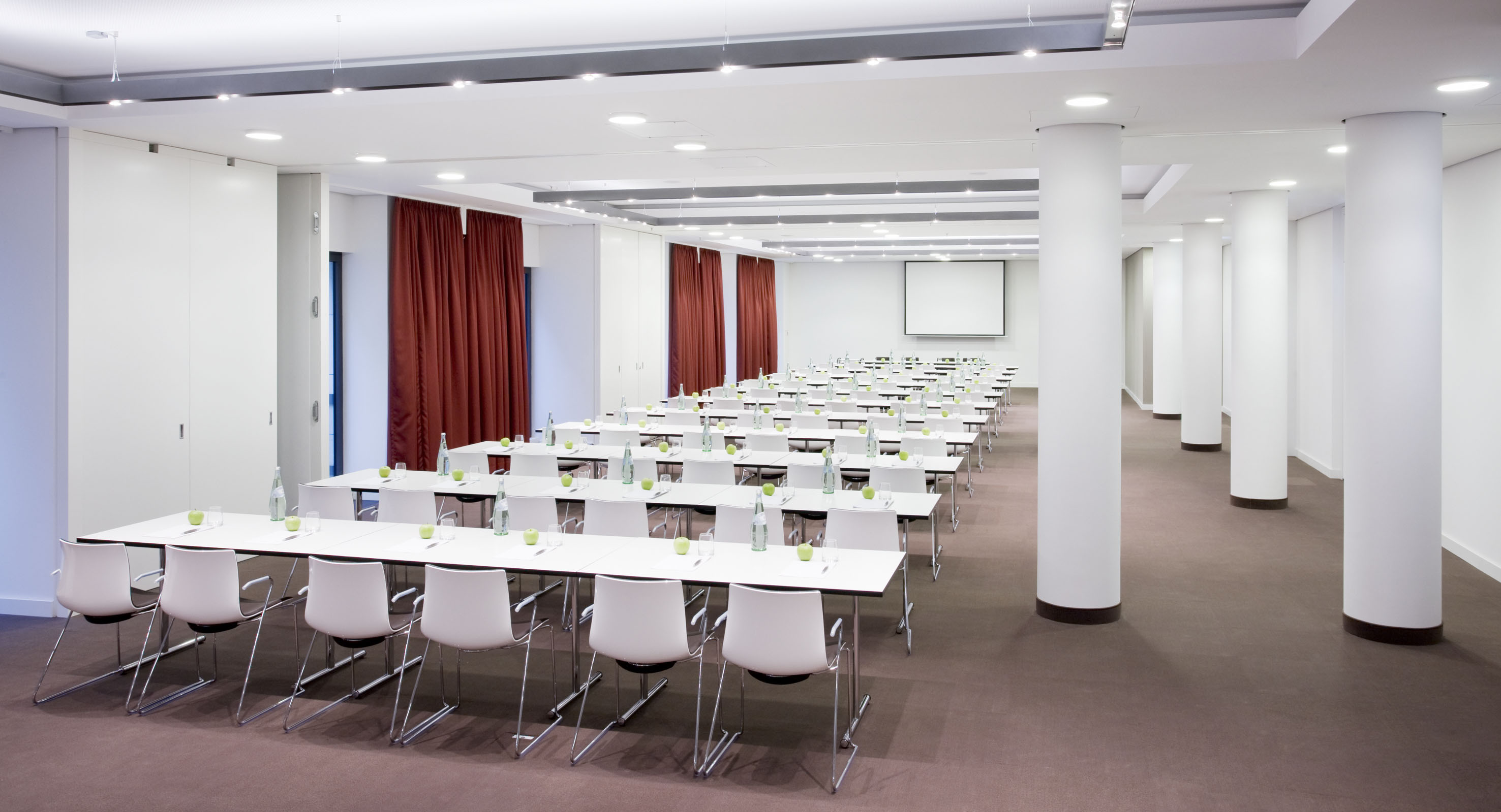 Classroom-style conference room with white tables, chairs, and a projection screen.