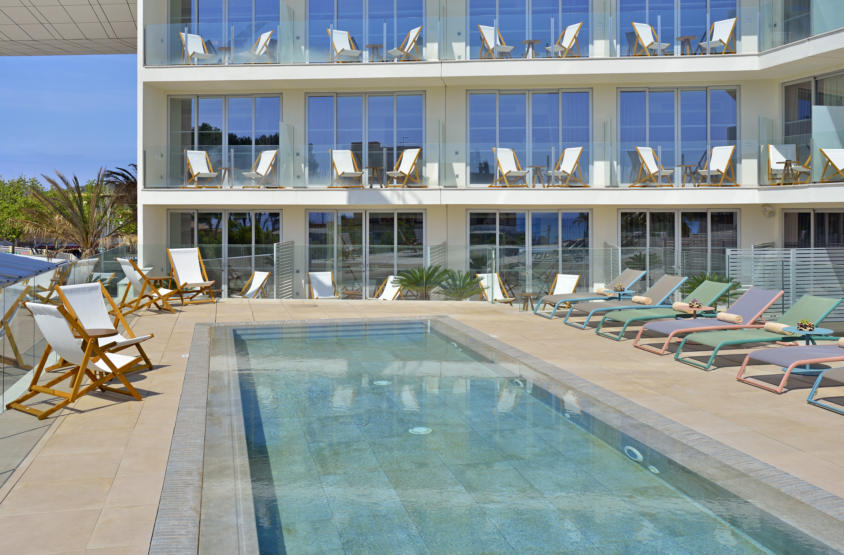 Hotel pool area with colorful sun loungers and modern building balconies.
