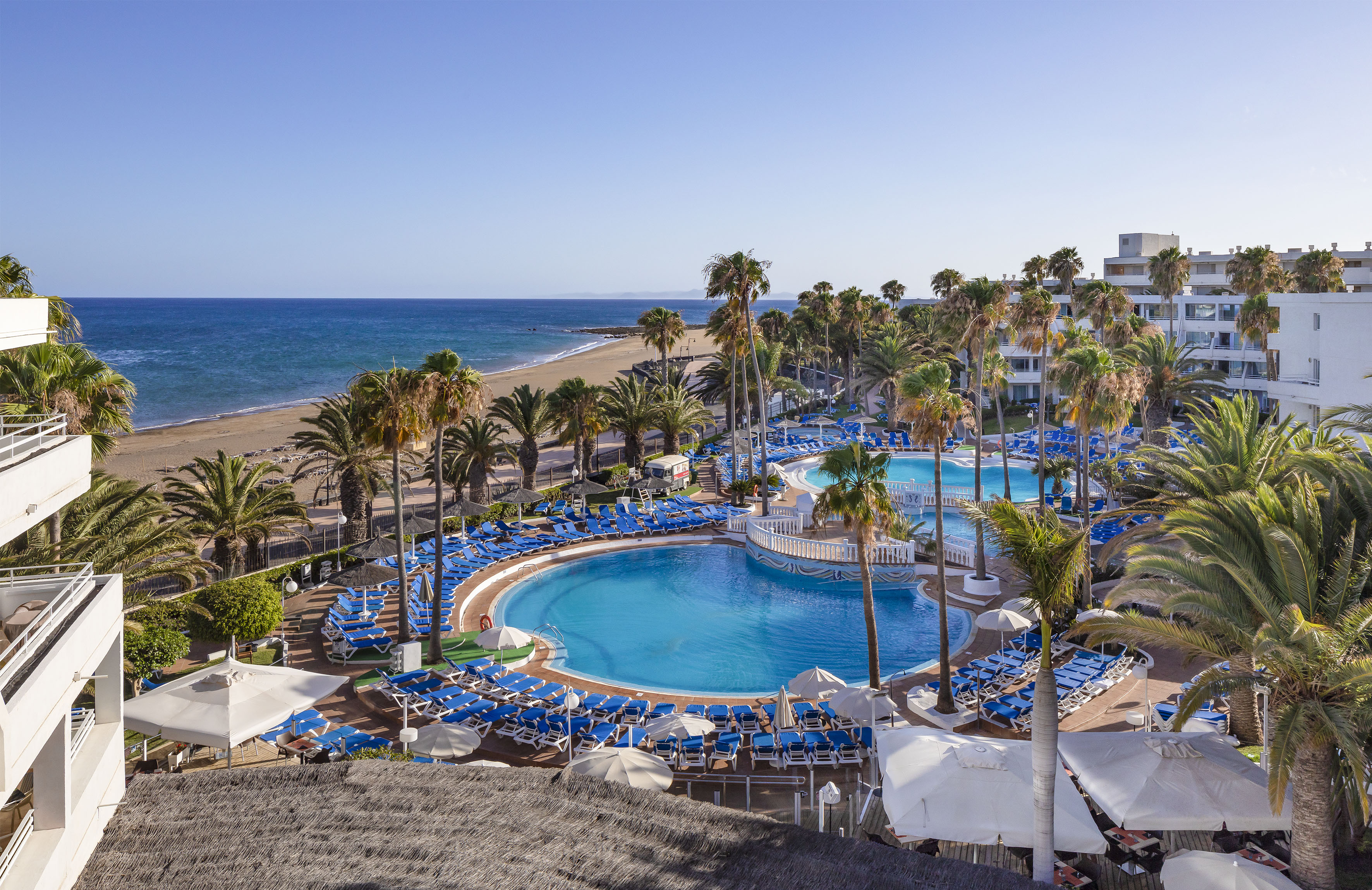 Beachfront resort with palm trees, multiple swimming pools, and ocean views.