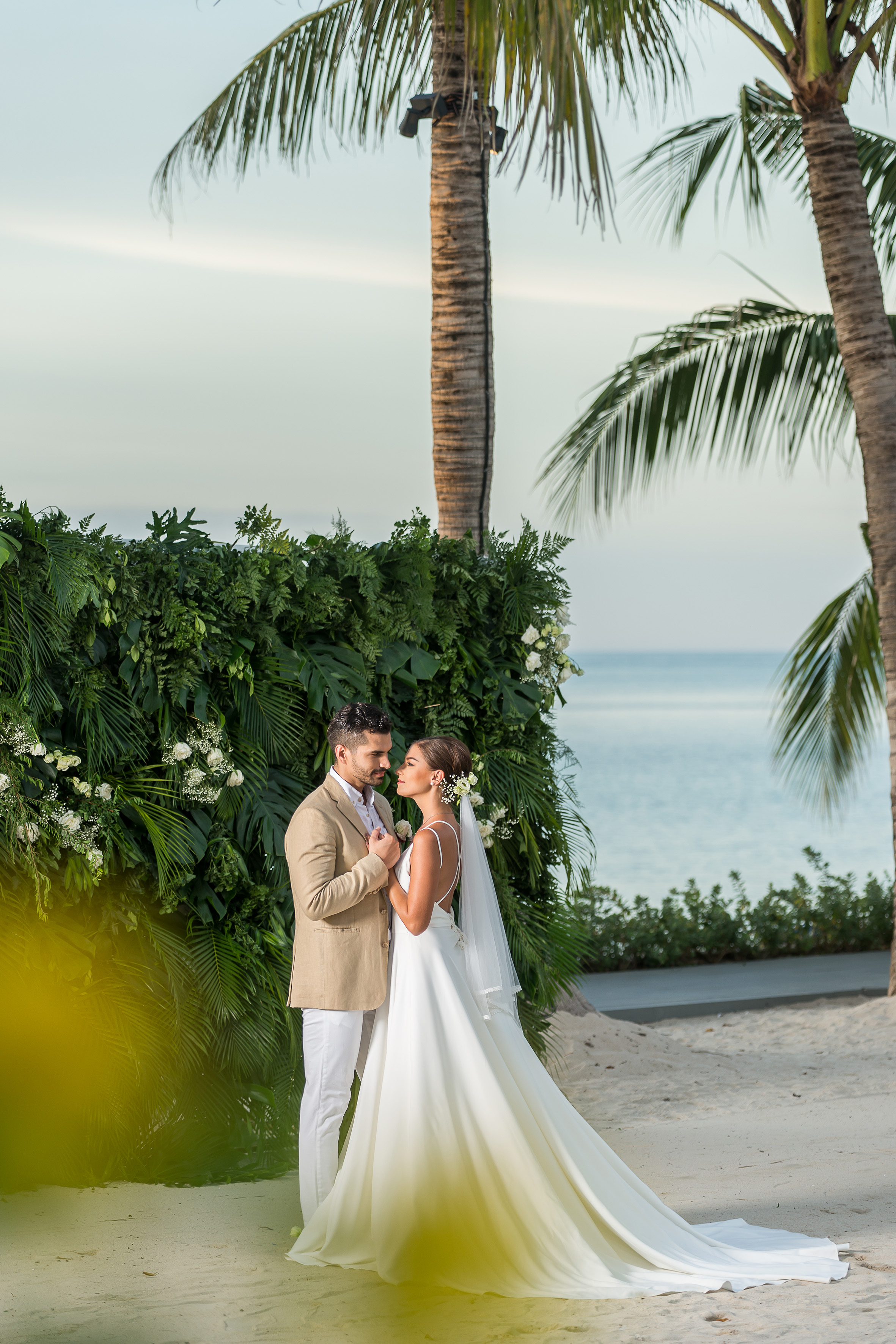 Bride and groom at a tropical beach wedding with ocean and palm trees.