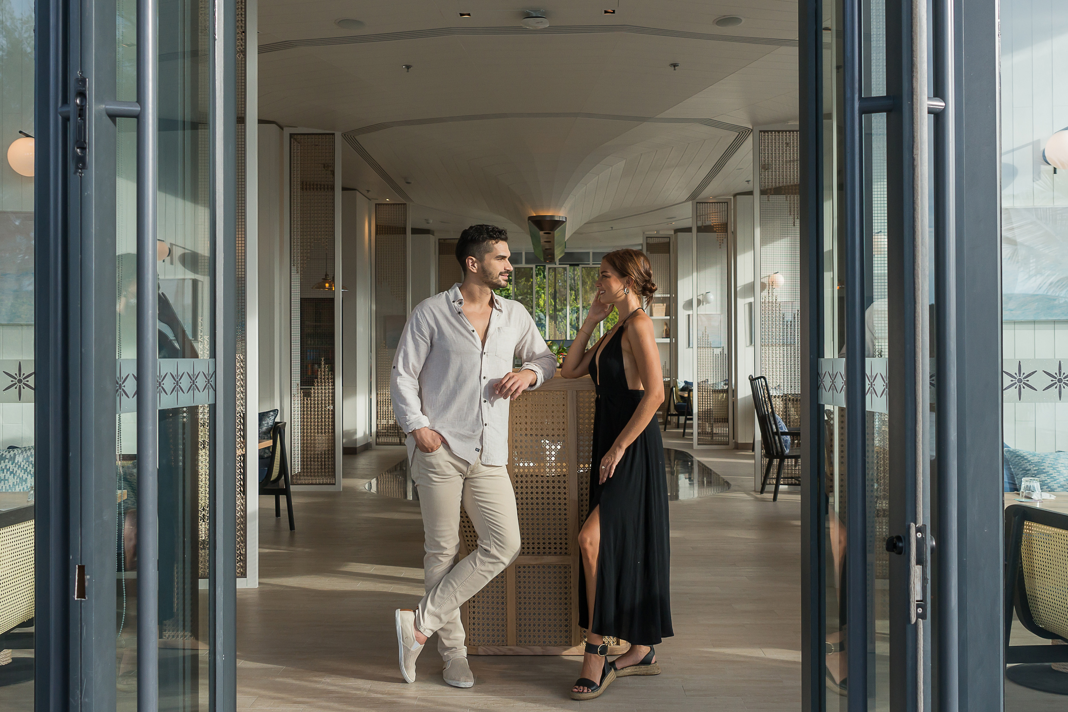 Stylish couple at entrance of a modern resort lounge, looking at each other.