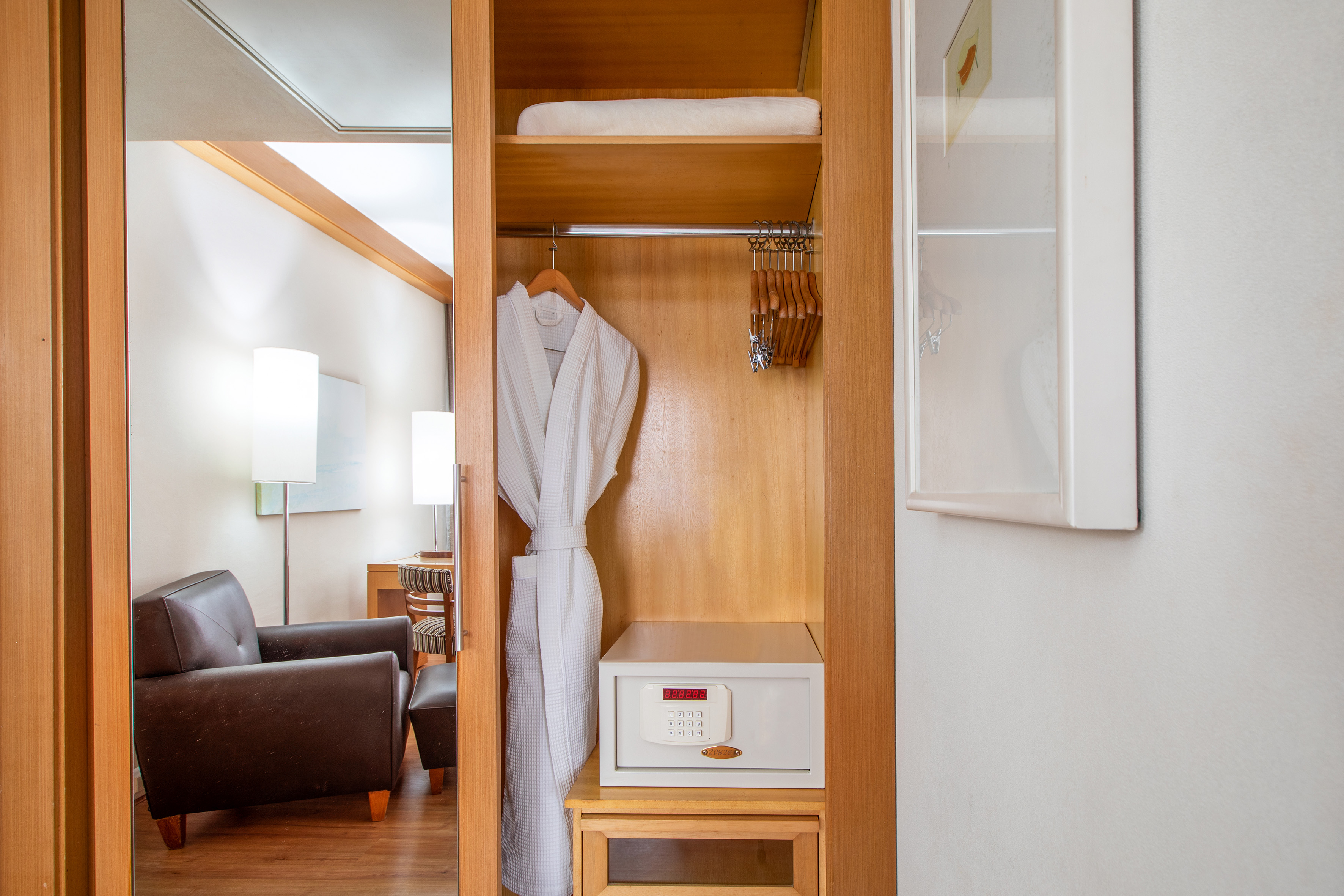 Hotel room closet with white bathrobe, safe, hangers, and towel.