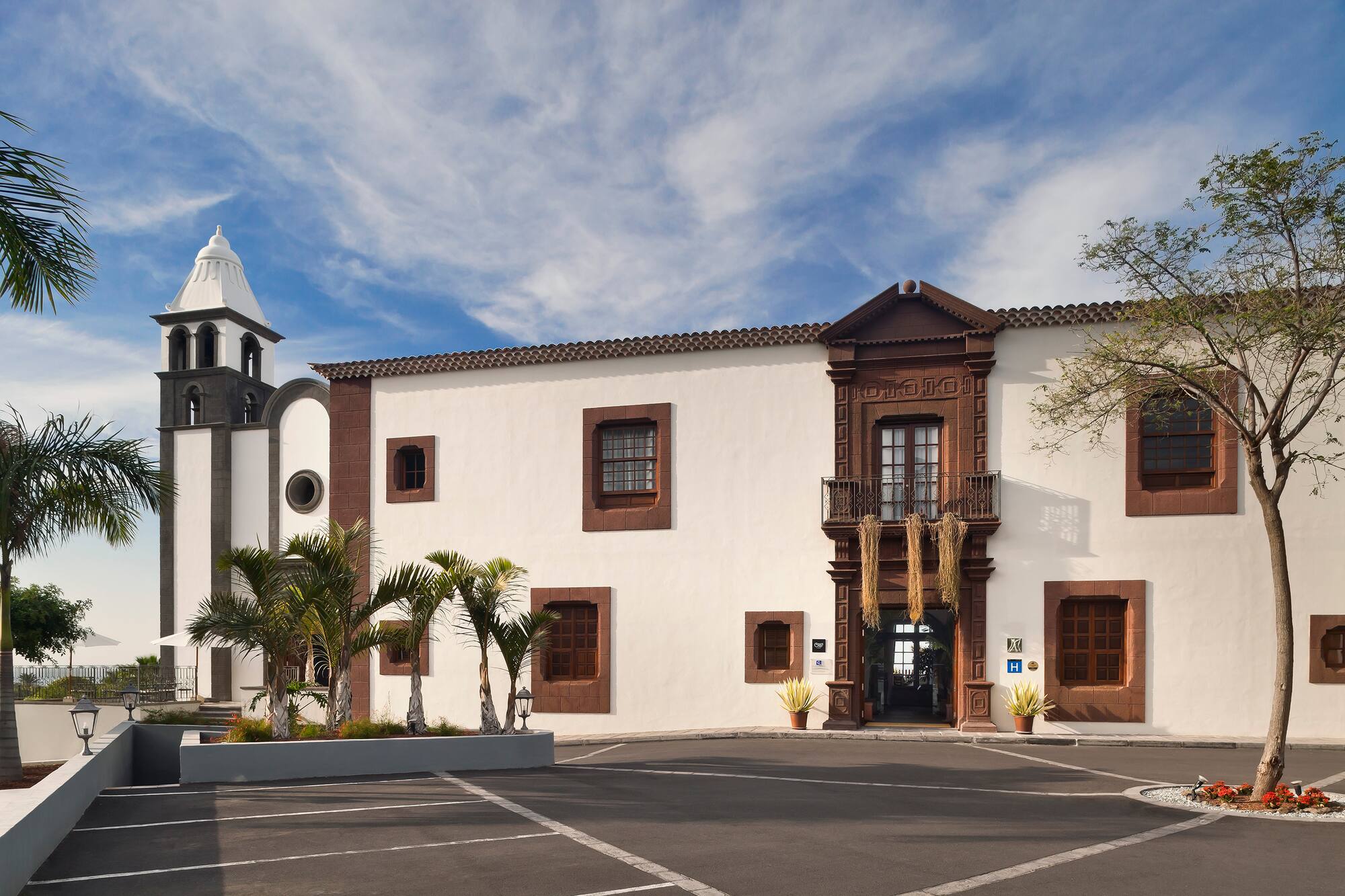Canarian style hotel with bell tower, ornate brown facade, and palm trees.