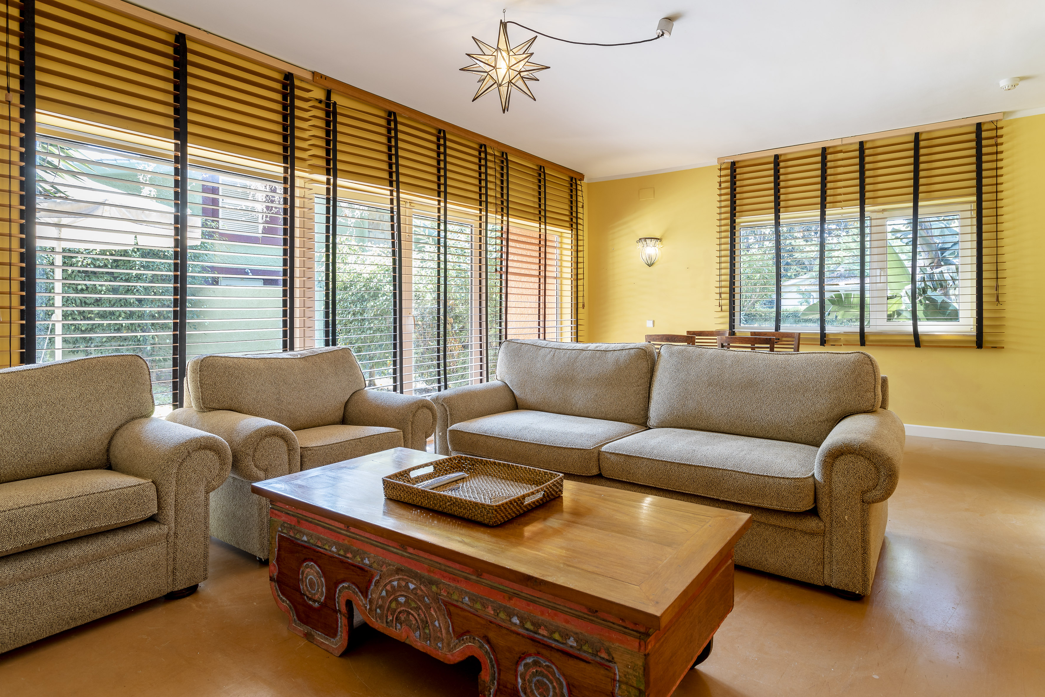 Bright yellow living room, beige couches, rustic coffee table, wood blinds.