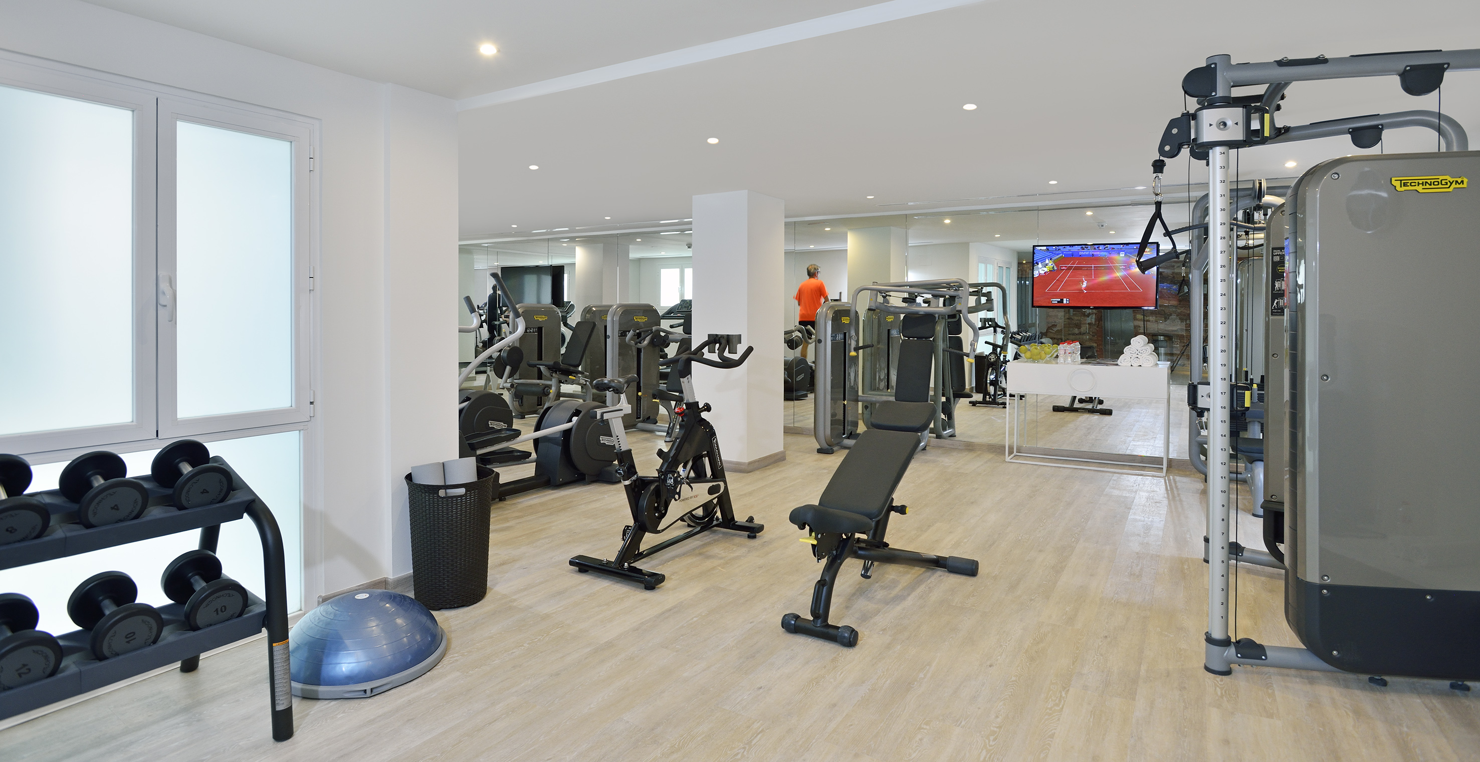 Well-equipped gym with cardio machines, weight rack, dumbbells, and bosu ball.