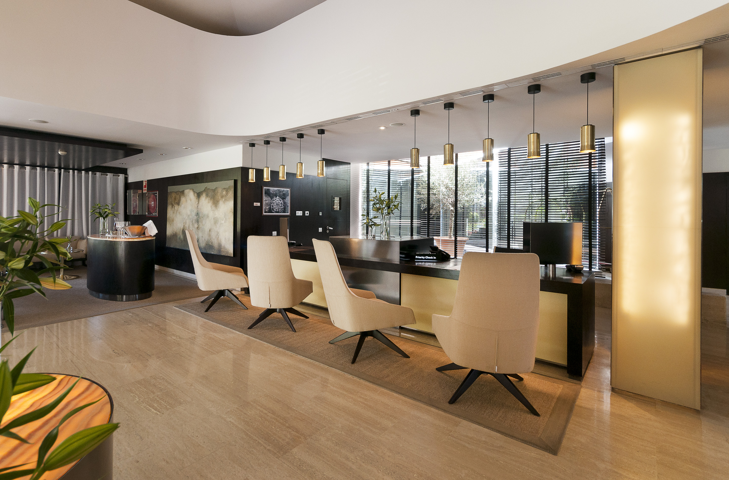 Modern hotel lobby with long reception desk, beige chairs, and gold pendant lights.