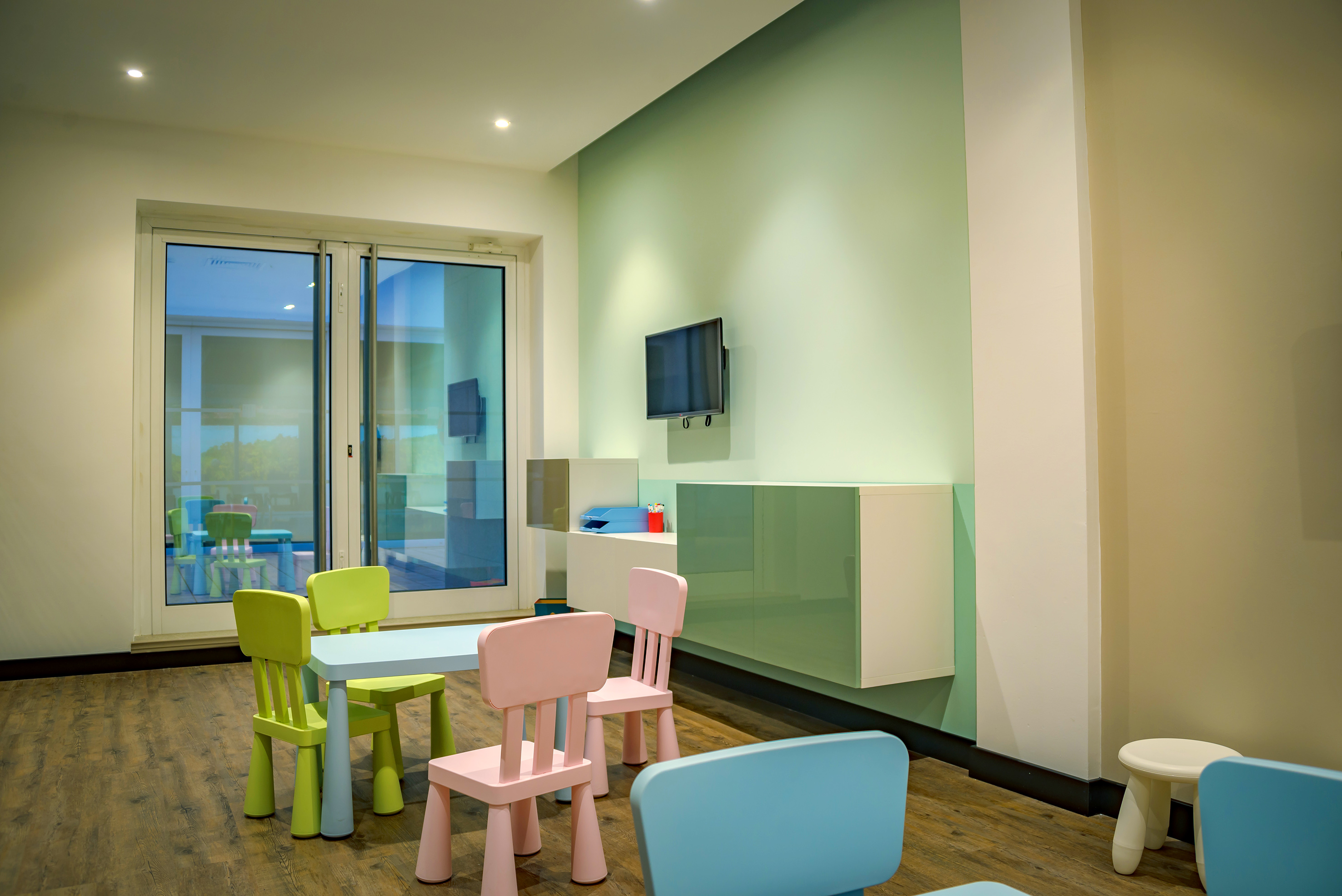Modern kids' playroom with colorful chairs, table, TV, and large windows.