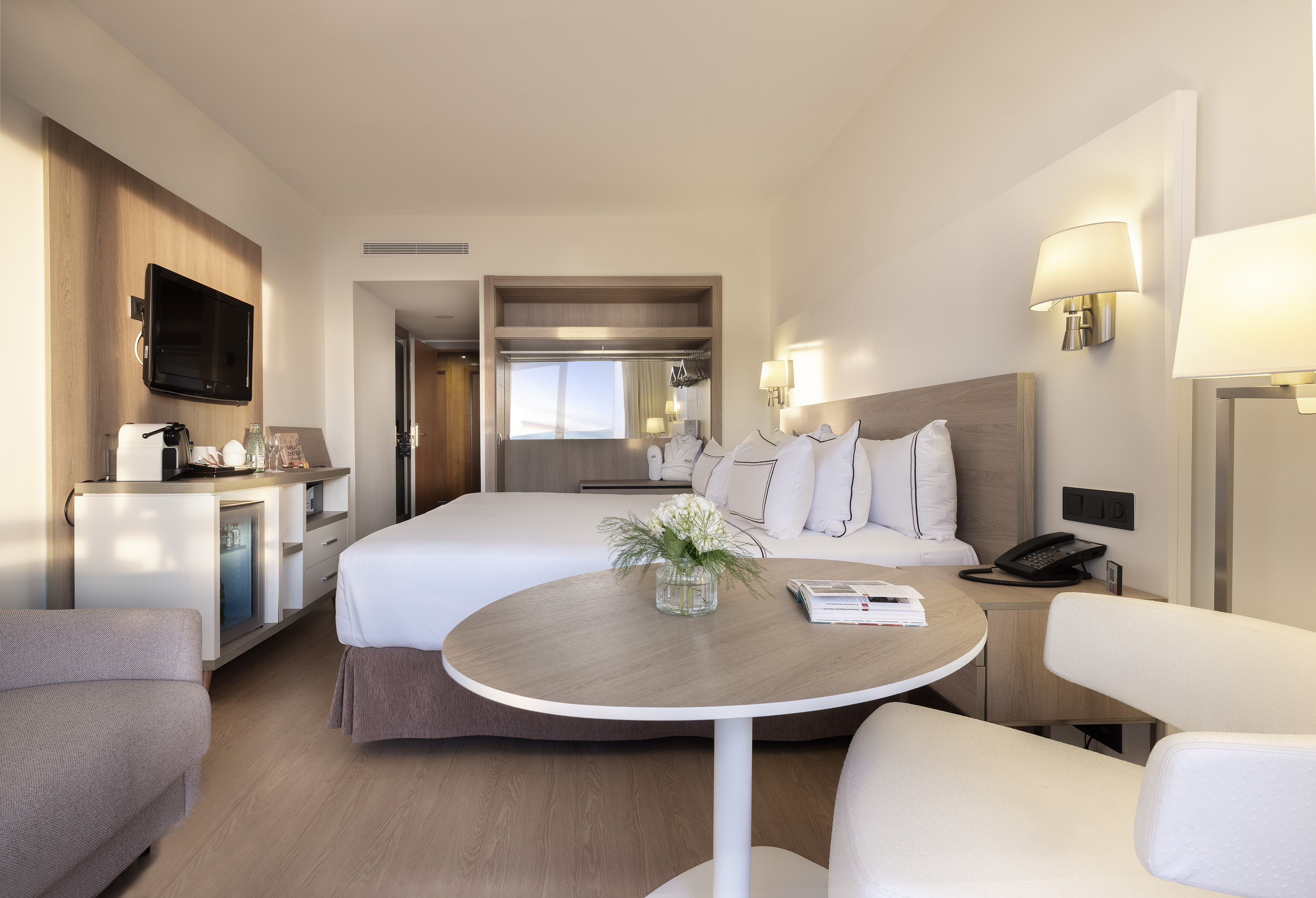Stylish hotel bedroom with a large bed, TV, coffee station, and cozy seating.