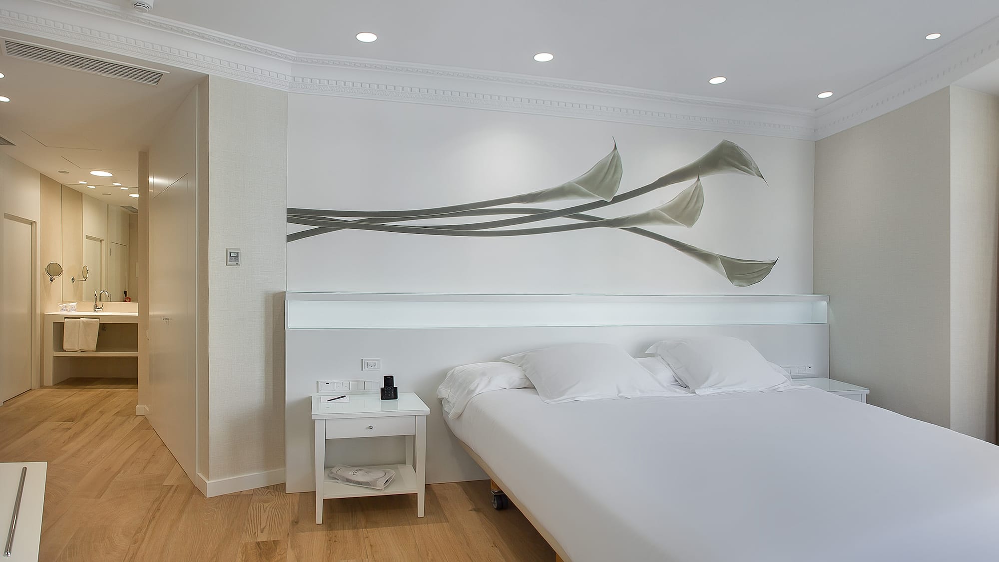 a bed with white sheets and pillows in a room with a white wall