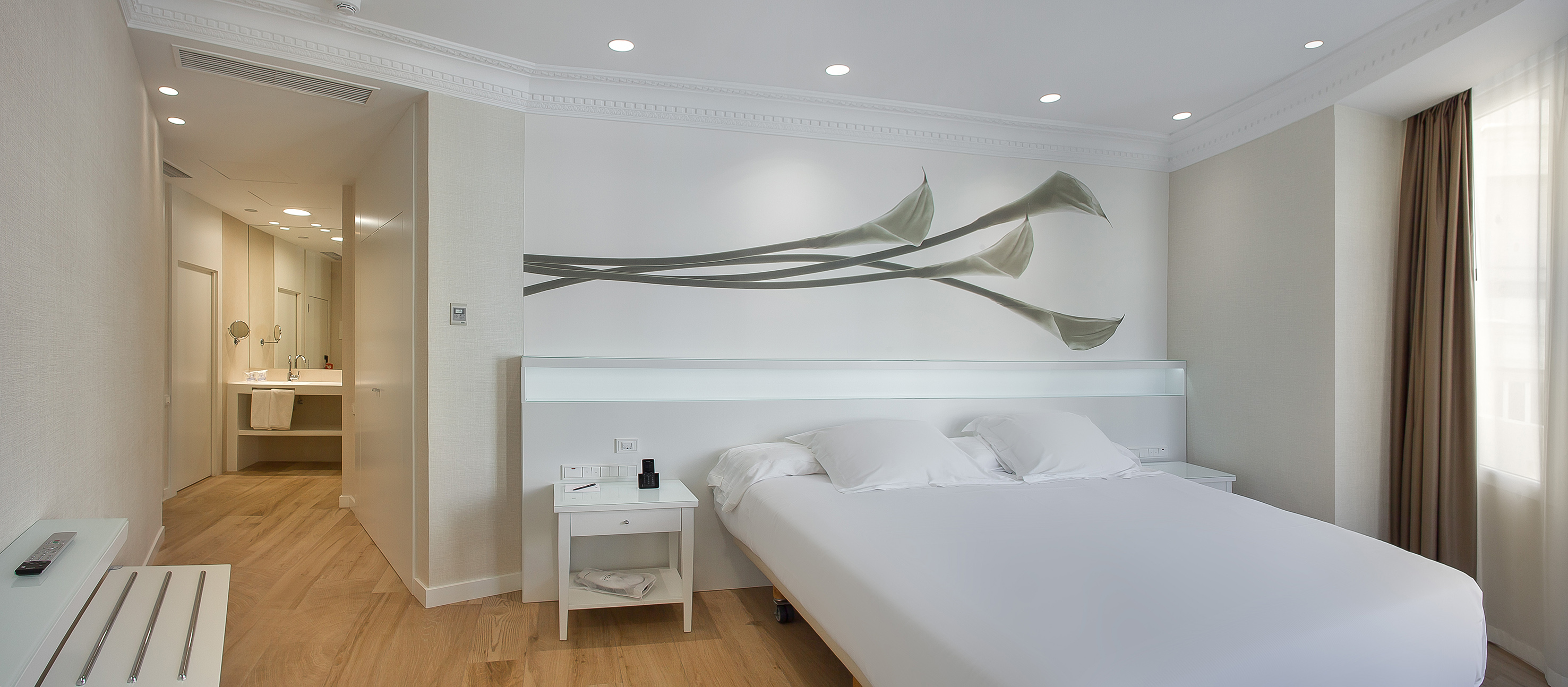 Modern hotel room with white bed, Calla lily art, and connecting bathroom.