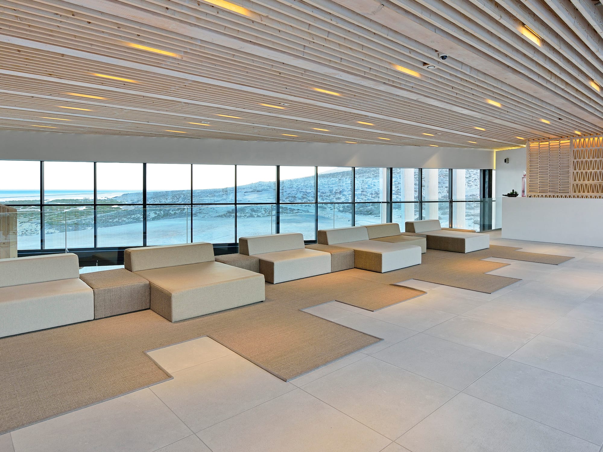 Coastal hotel lobby with ocean view, modular seating, and wooden ceiling.