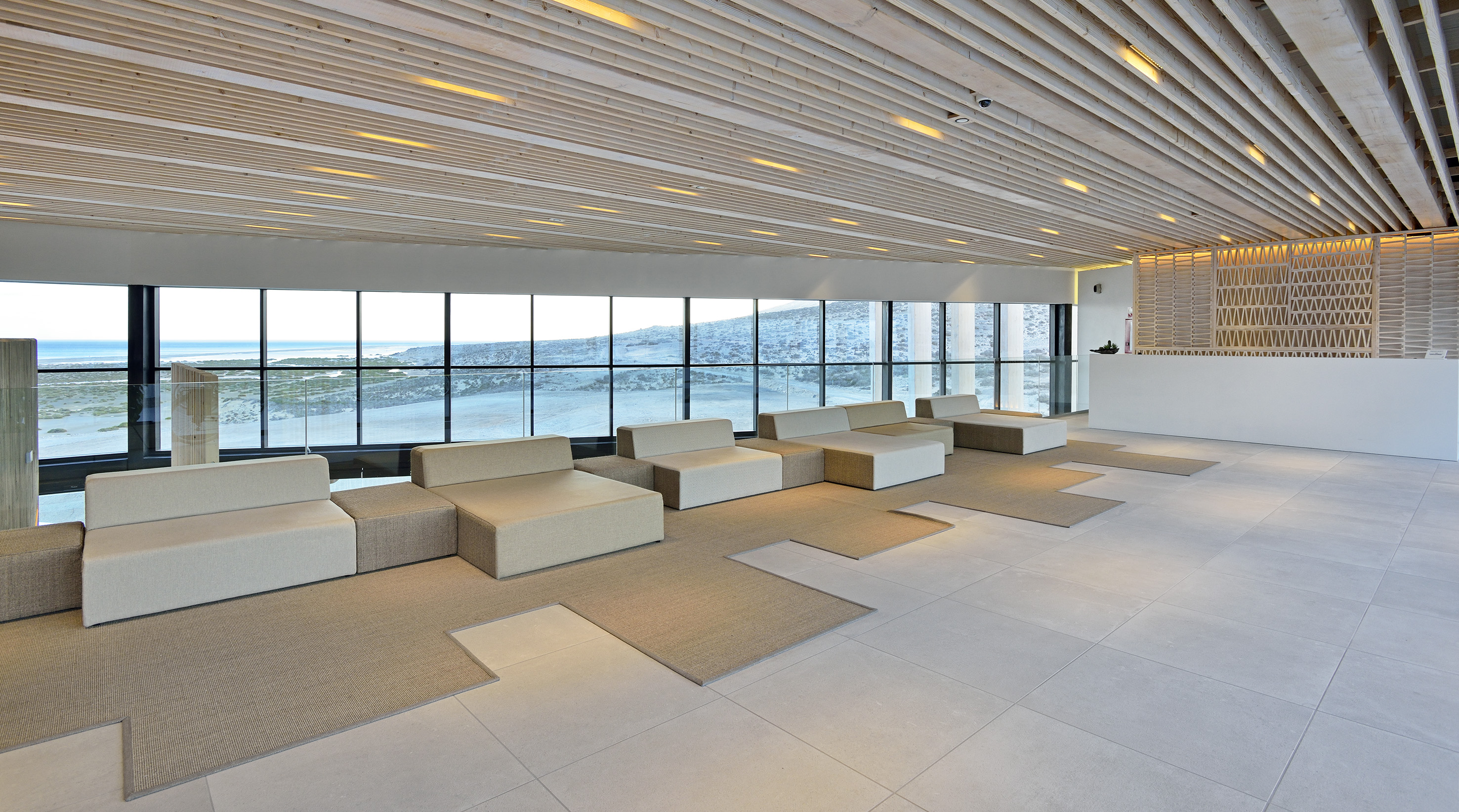 Coastal hotel lobby with ocean view, modular seating, and wooden ceiling.
