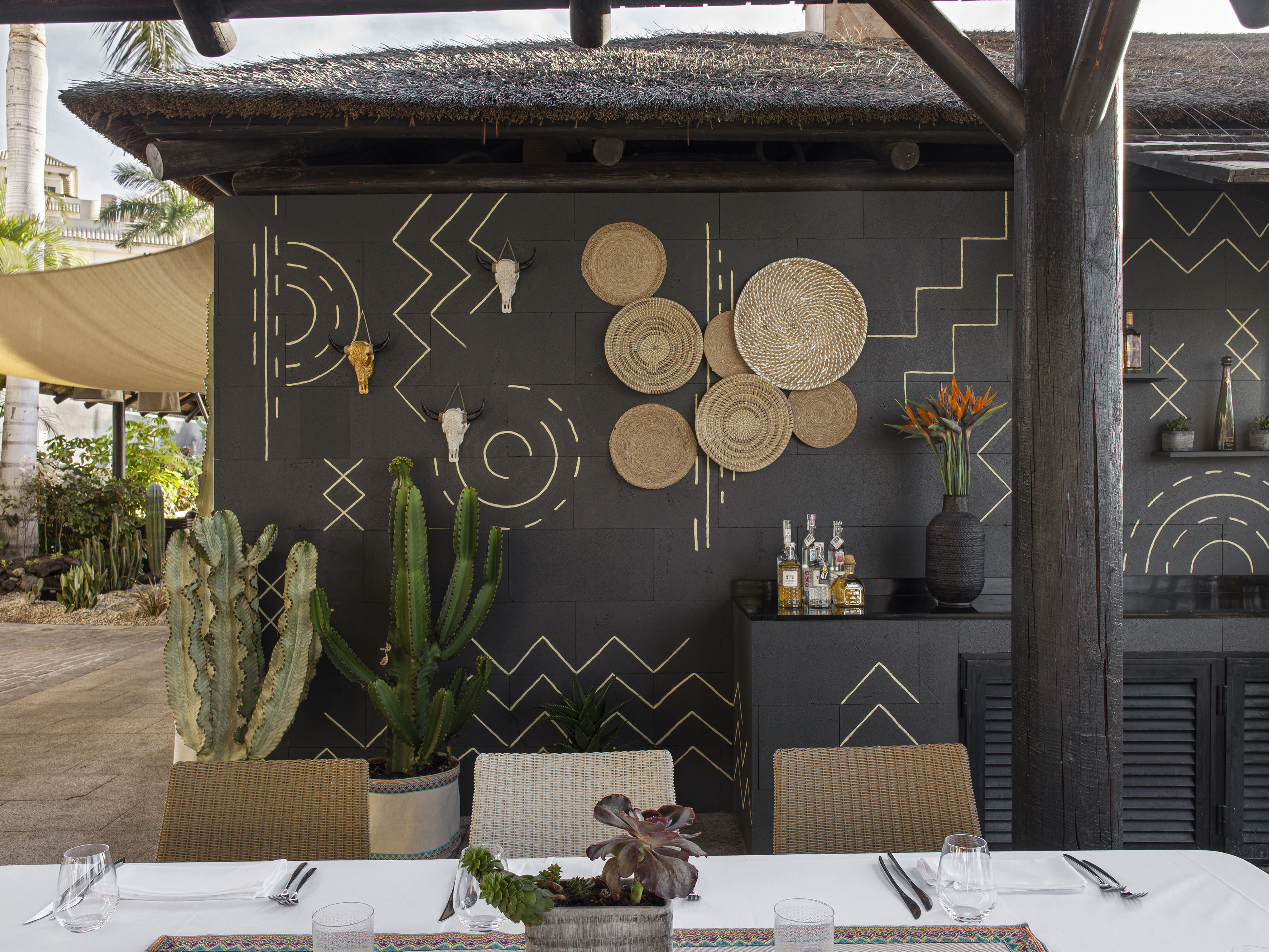 Bohemian outdoor restaurant patio with patterned wall, woven decor, and cacti.