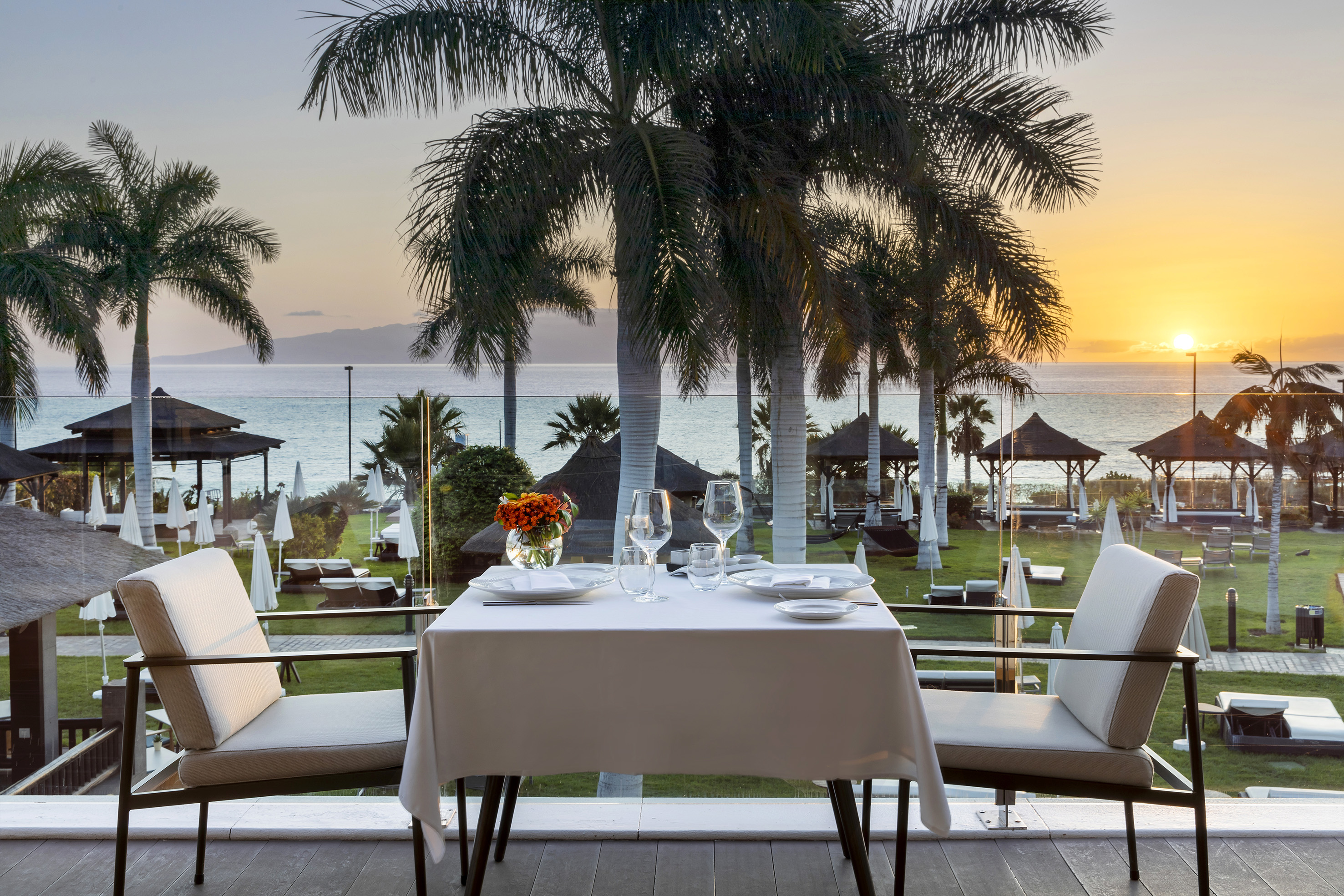 a table with plates and flowers on it and chairs on a deck with a view of the ocean