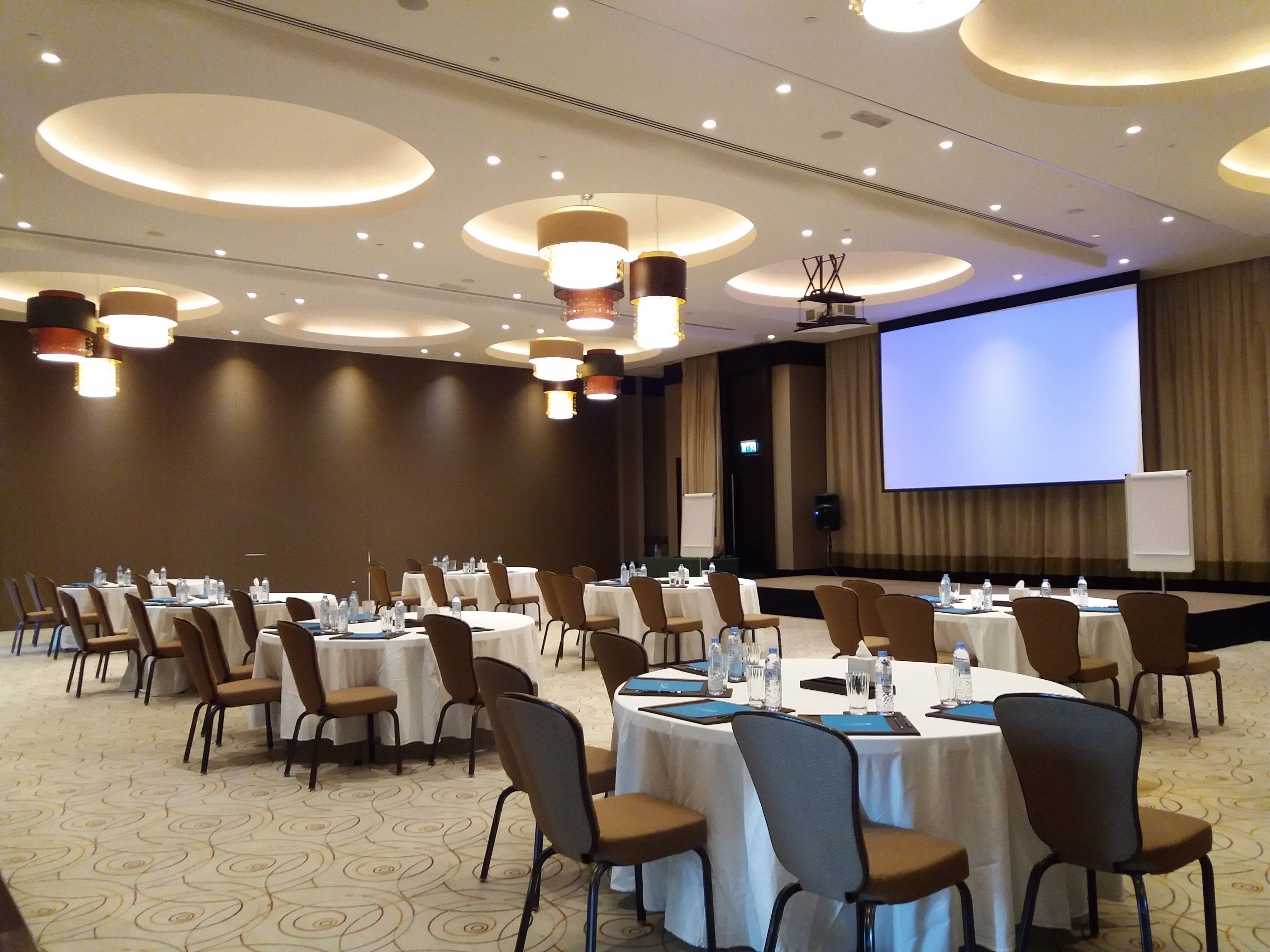 Conference room with round tables, projector screen, and modern lights.